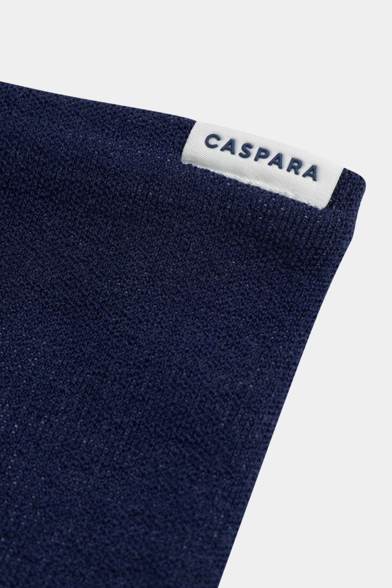 Close-up of the navy CASPARA Classic Neckwarmer showing knit texture and white logo label.