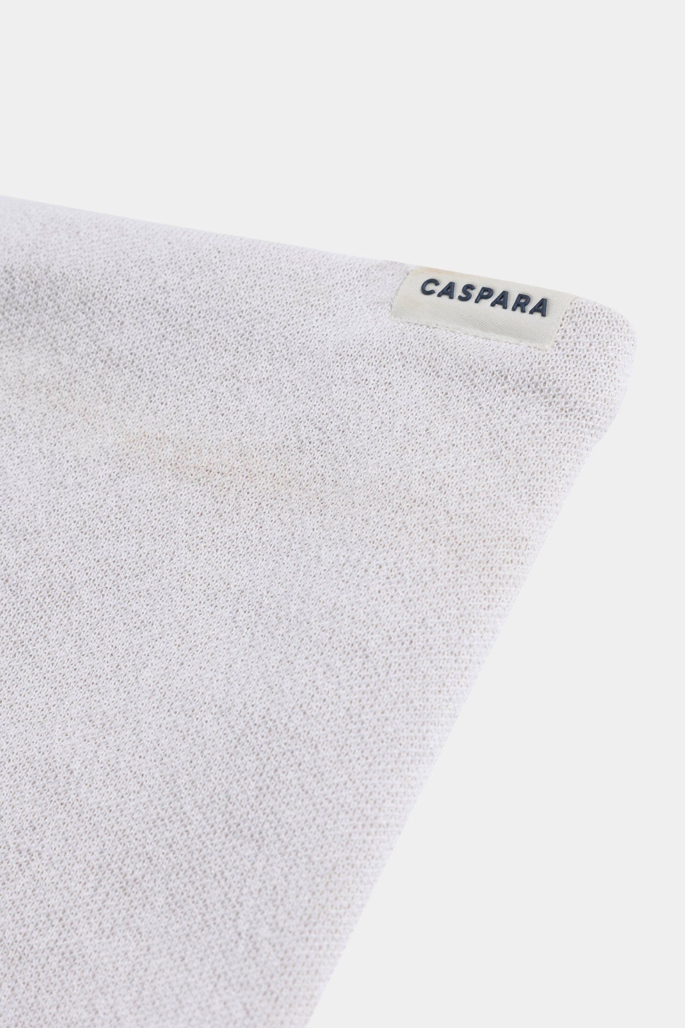 Close-up of the creme knit fabric and CASPARA logo tag on the Classic Neckwarmer.