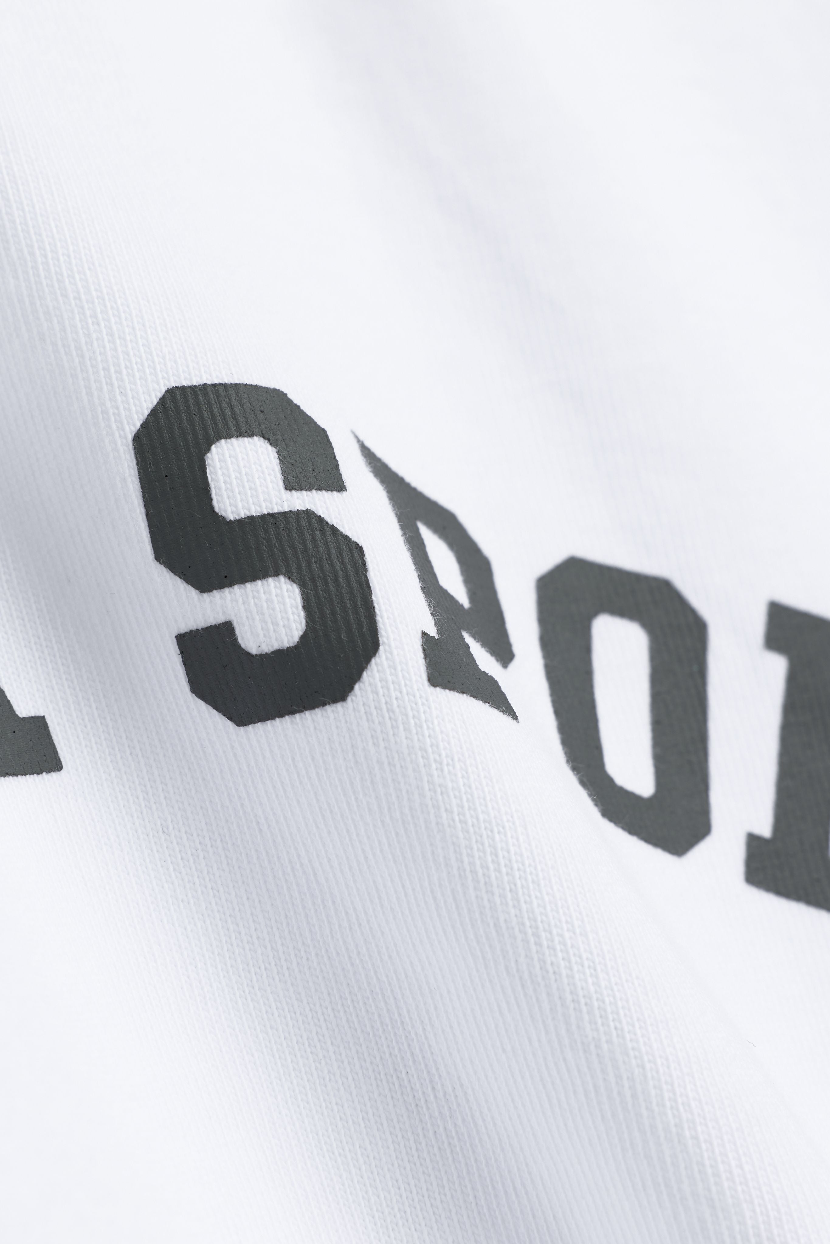 Close-up of the khaki graphic print on a white CASPARA CS Signature cotton tee.