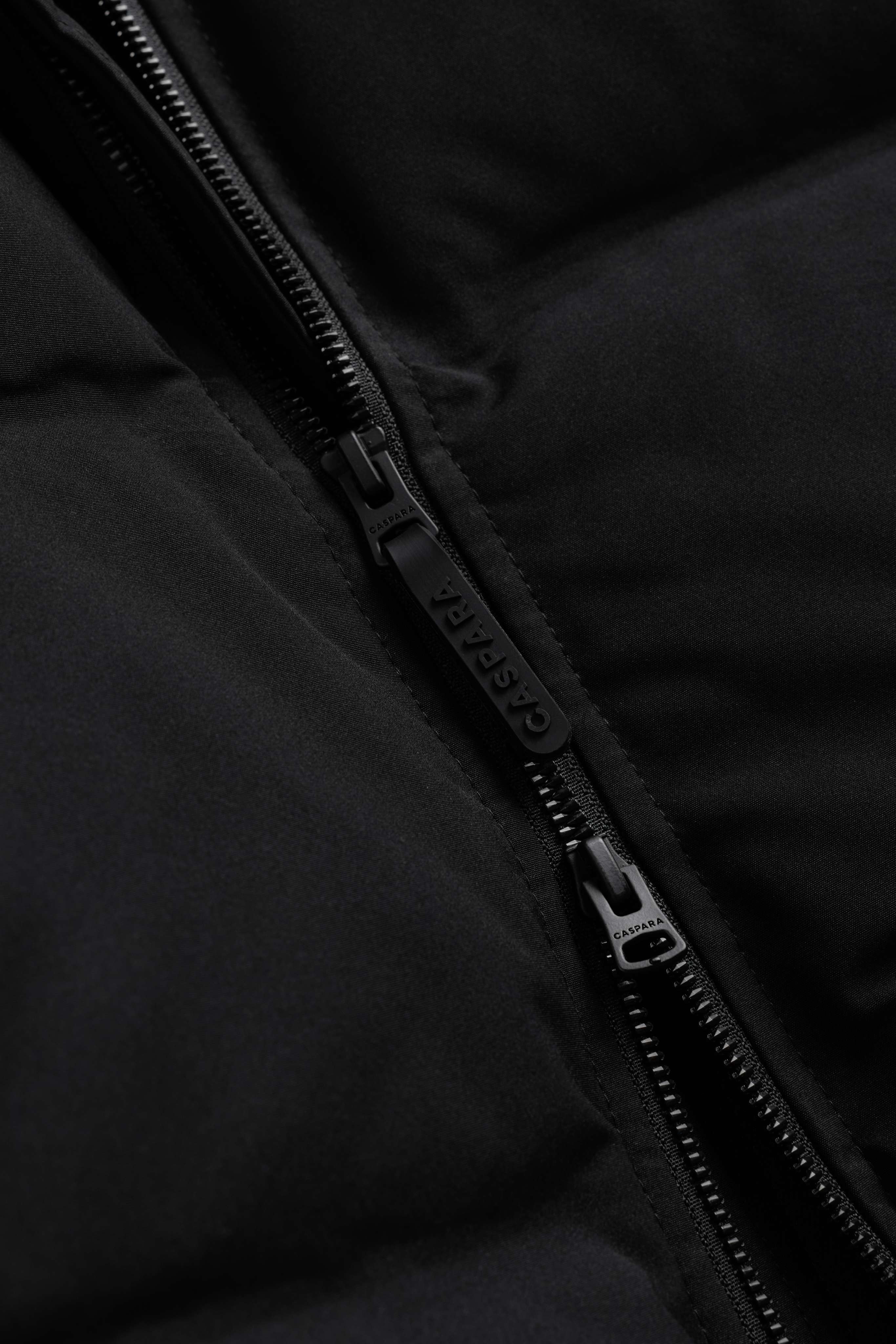 Close-up of the branded two-way zipper on the black CASPARA Boreal Puffer Jacket.