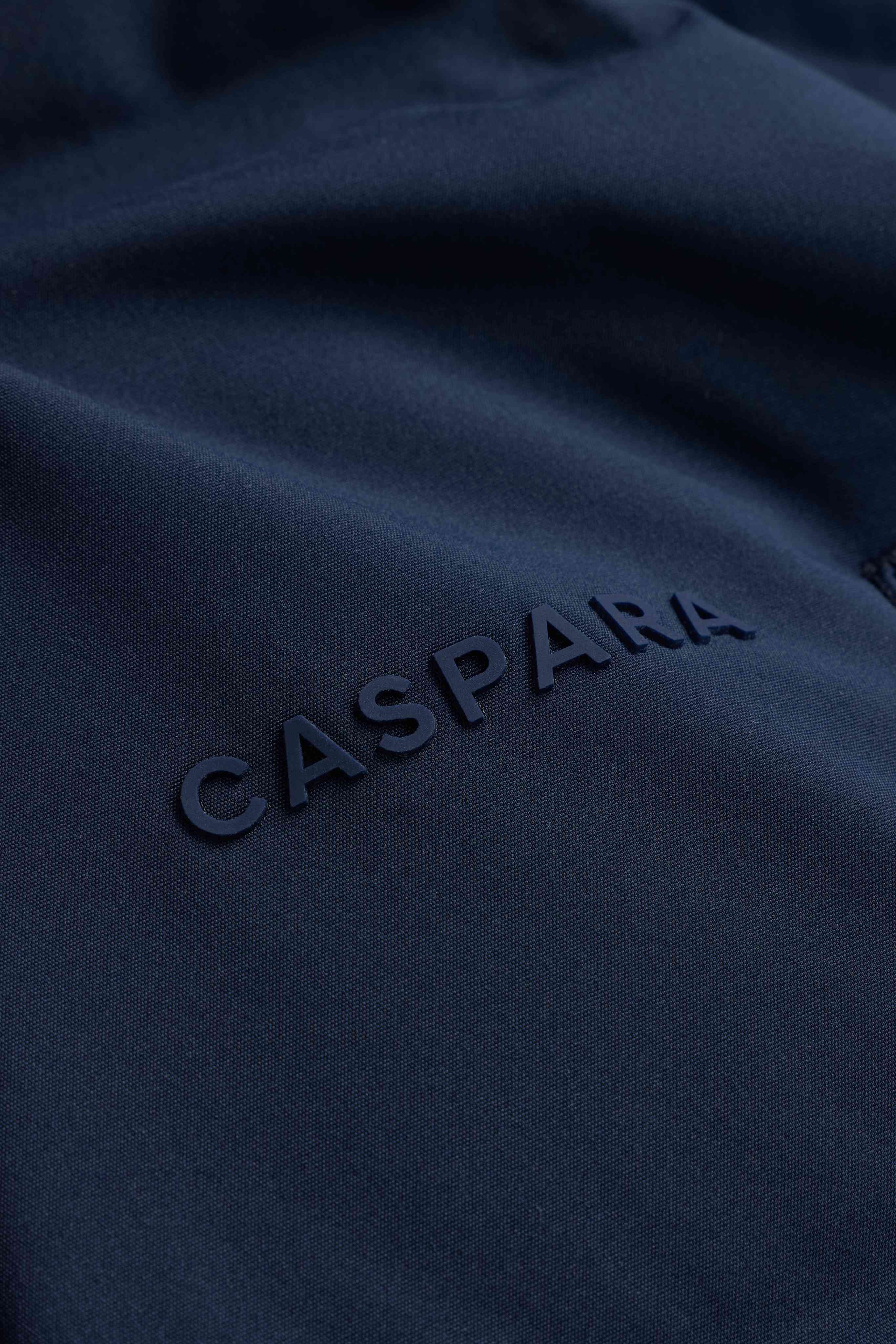 Close-up of the embossed CASPARA logo on the navy Boreal puffer jacket.
