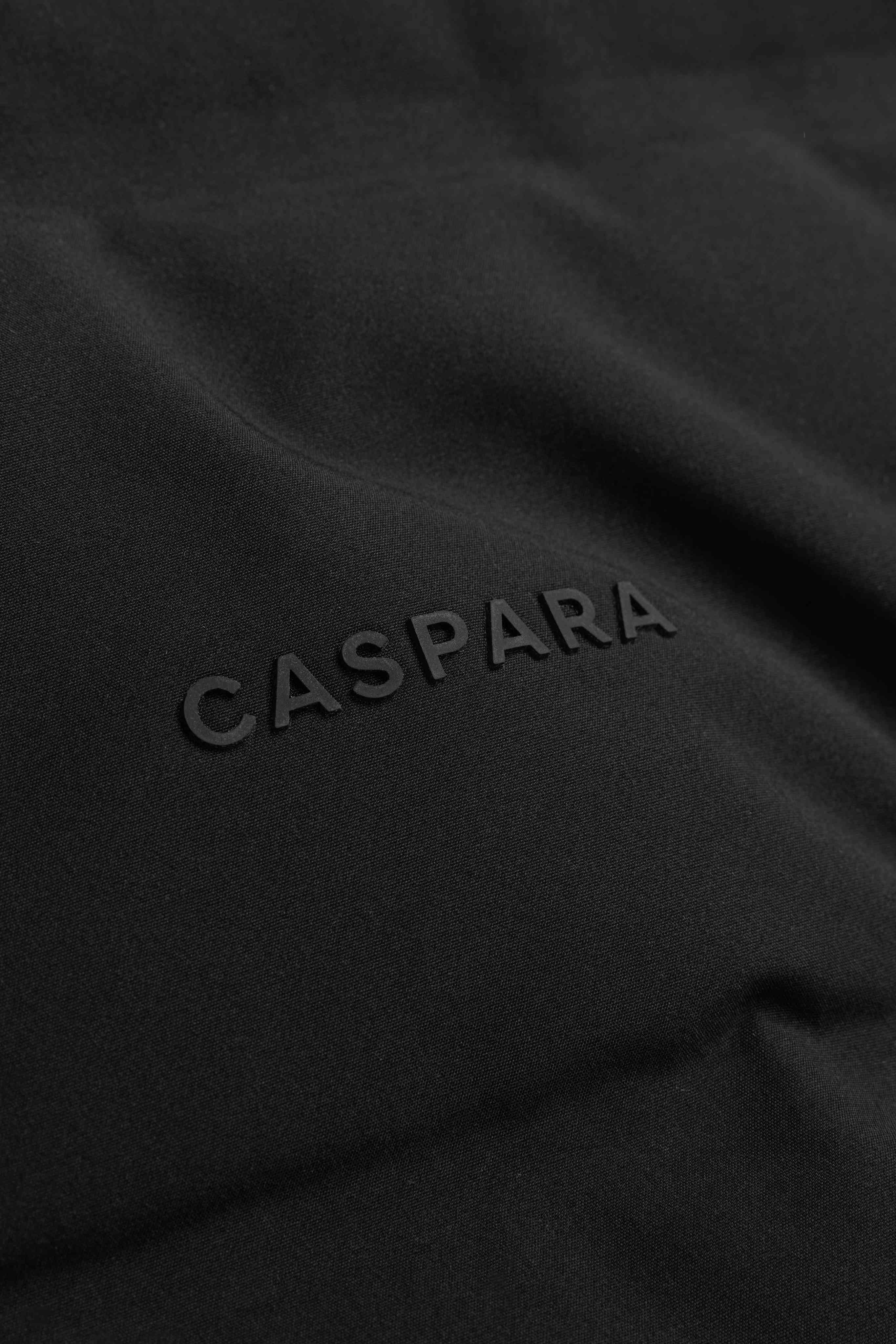 Close-up of the tonal CASPARA logo on the black Aurora puffer jacket.