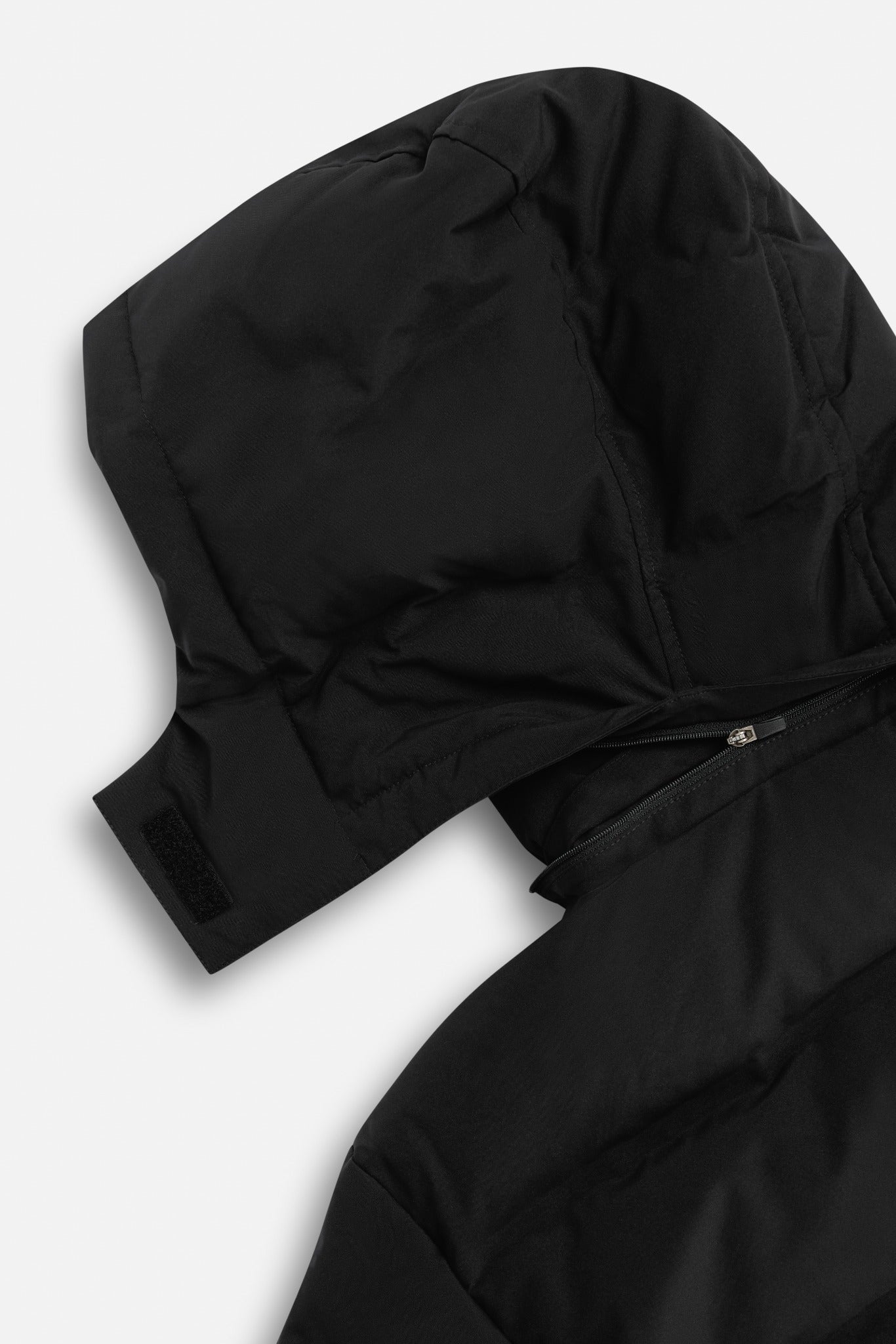 Close-up of the detachable hood and zipper on a black CASPARA puffer jacket.