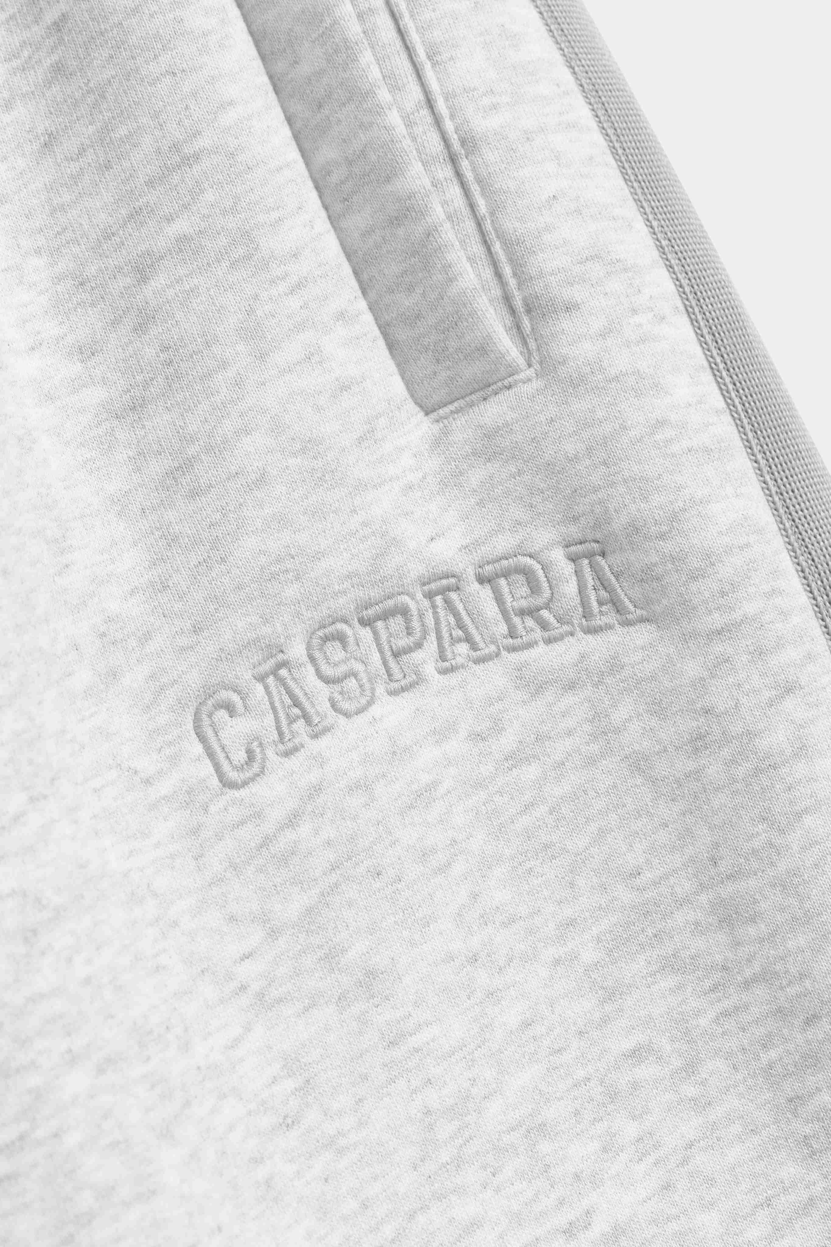 Close-up of embroidered CASPARA logo and piping detail on grey melange All-Star sweatpants.