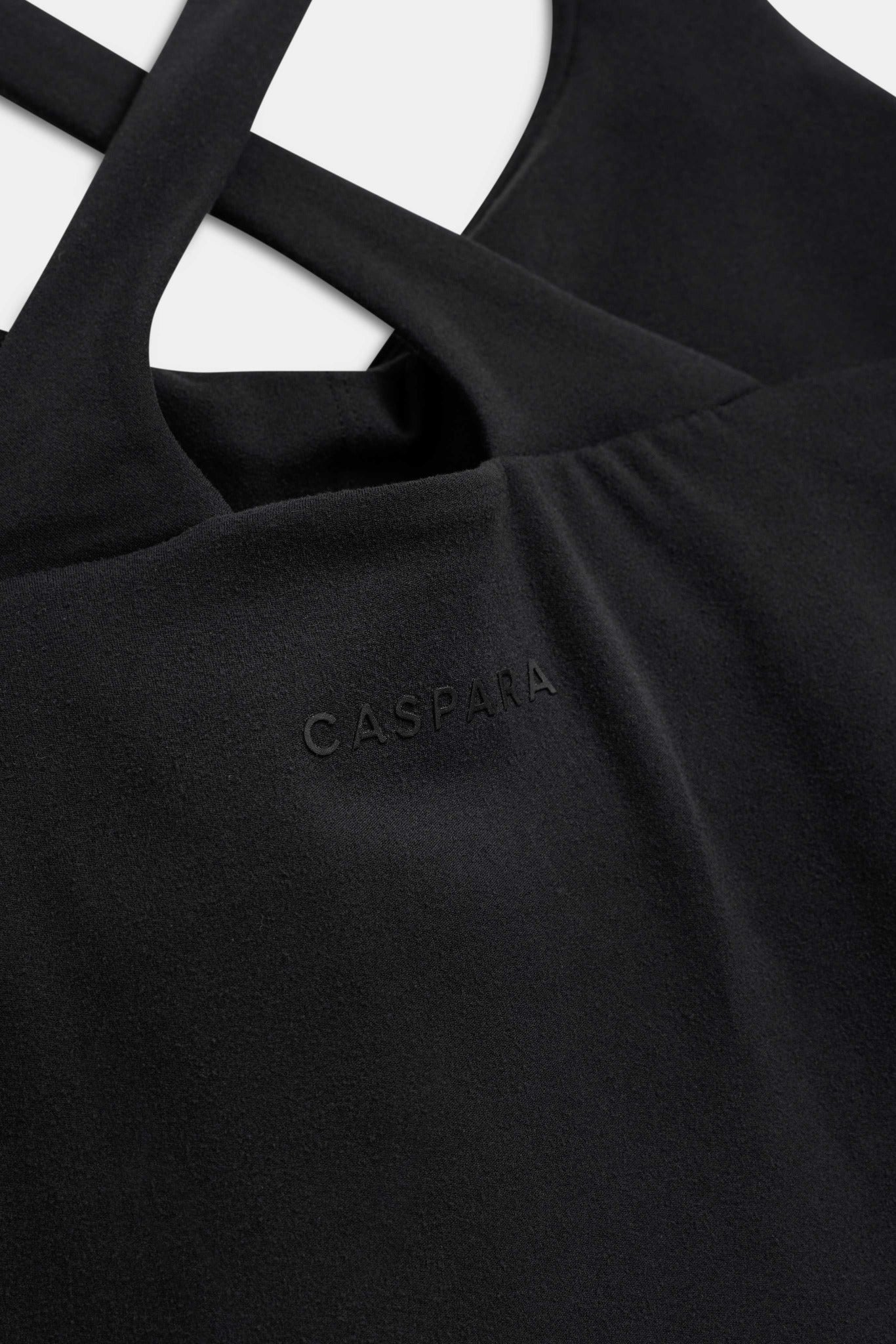 Close-up of the black CASPARA Cloudform top showing crossback straps and raised rubber logo.
