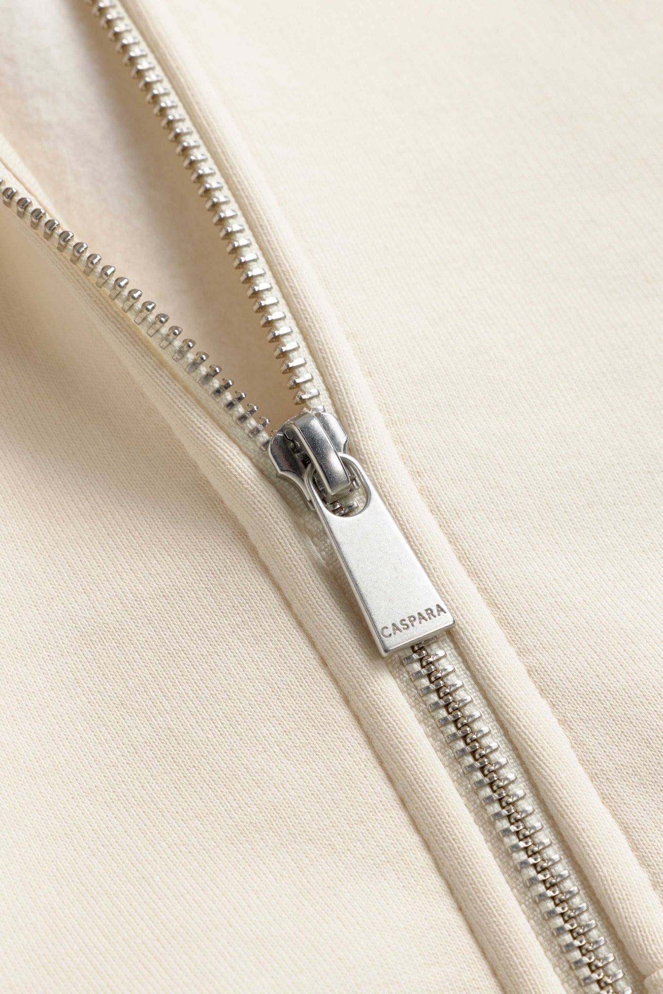 Close-up of the silver CASPARA engraved zipper pull on a creme zip hoodie.