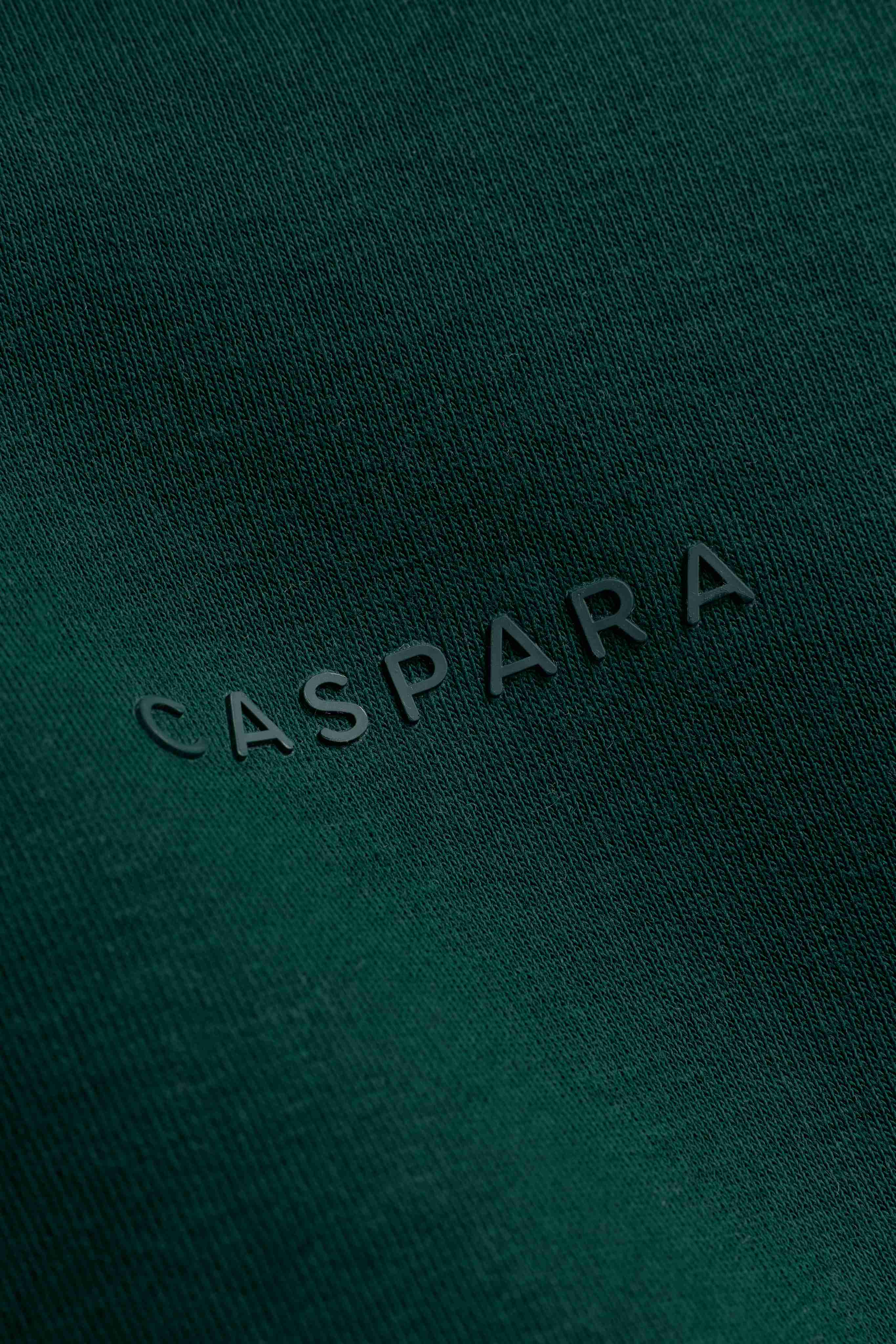 Close-up of the tone-in-tone CASPARA logo on racing green cotton hoodie fabric.