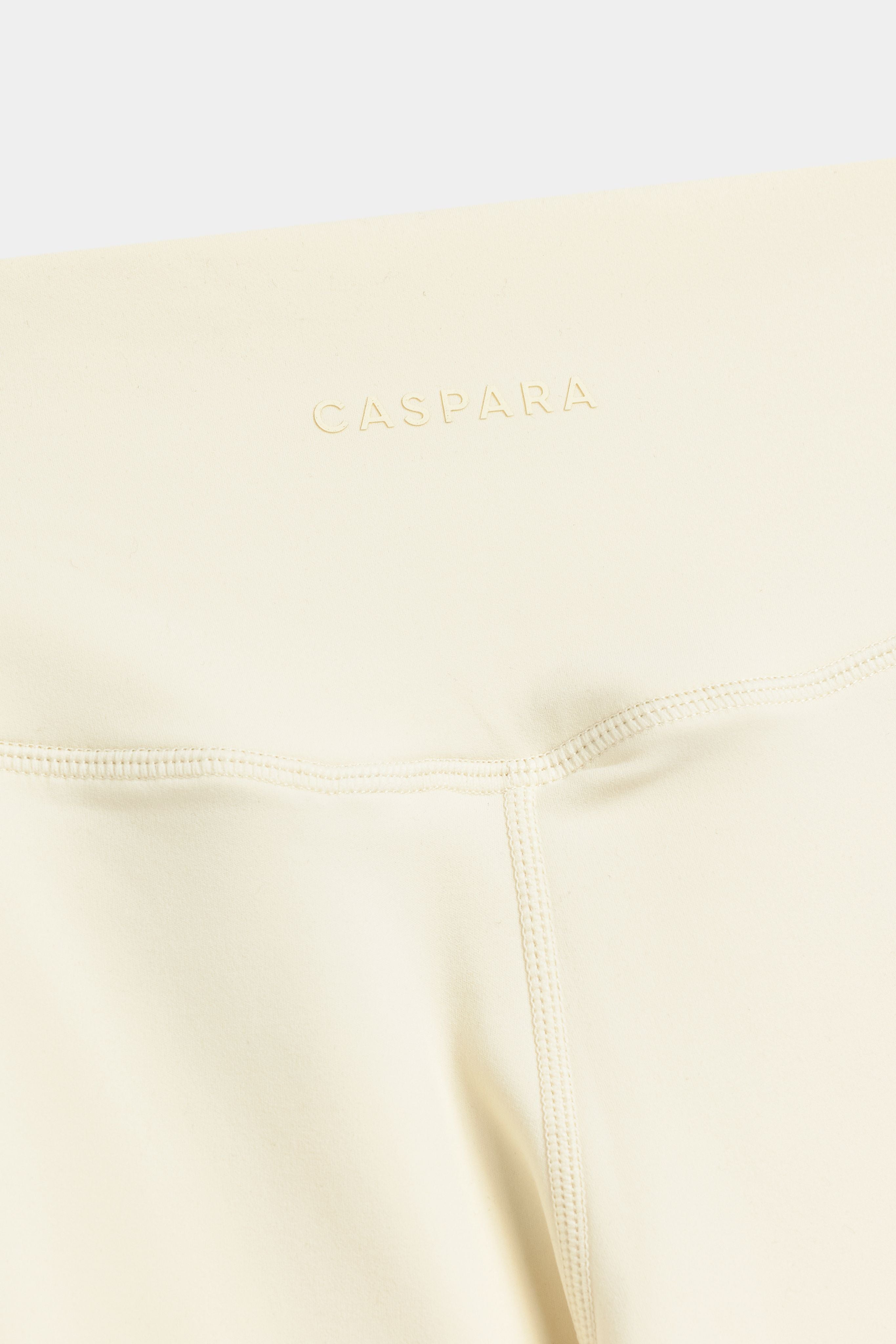 Close-up of the raised tonal CASPARA logo on butter yellow Cloudform yoga pants.