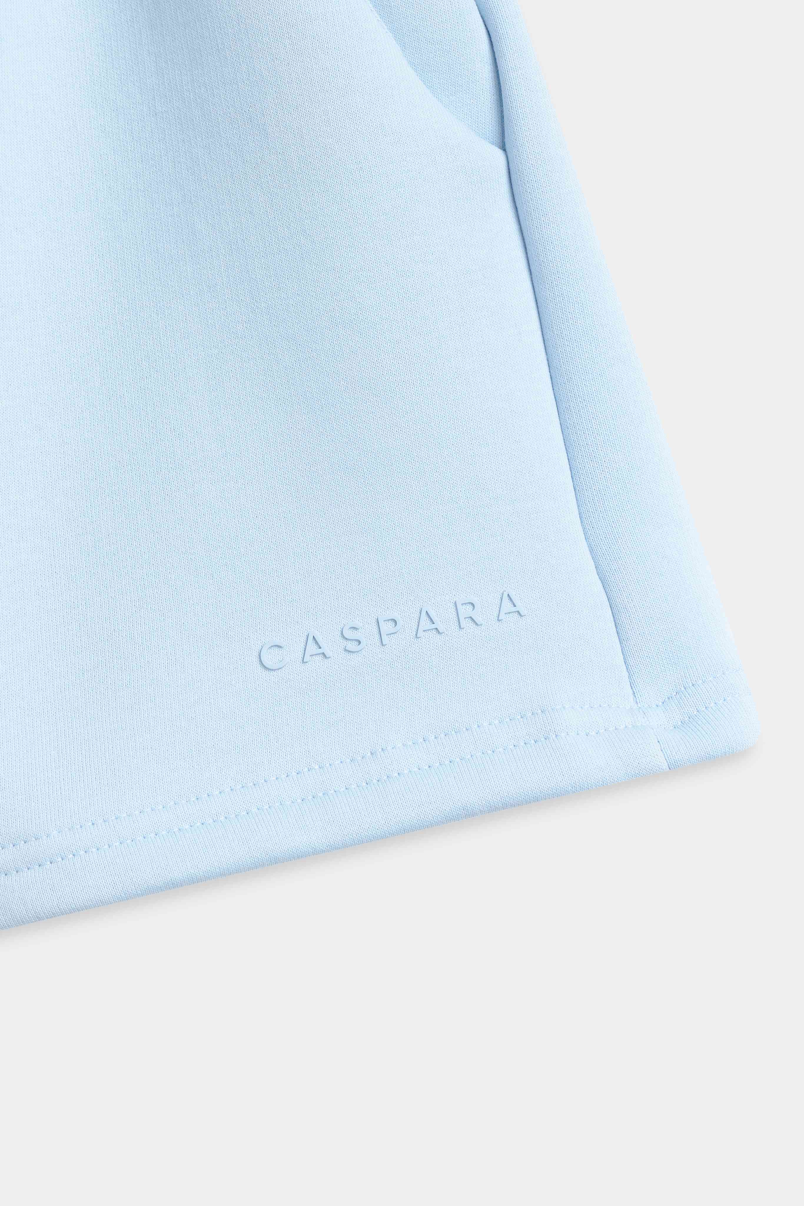 Close-up of the tone-in-tone CASPARA rubber logo on baby blue Pollux shorts.