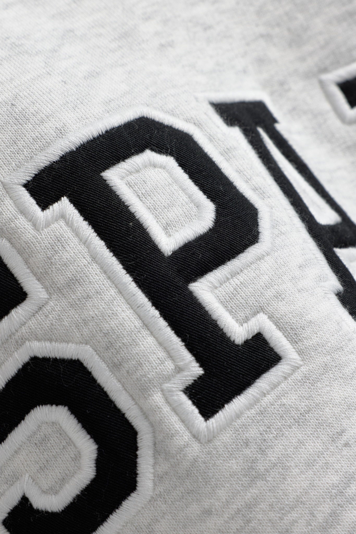 Close-up of the black and white embroidered CASPARA logo on a grey melange hoodie.
