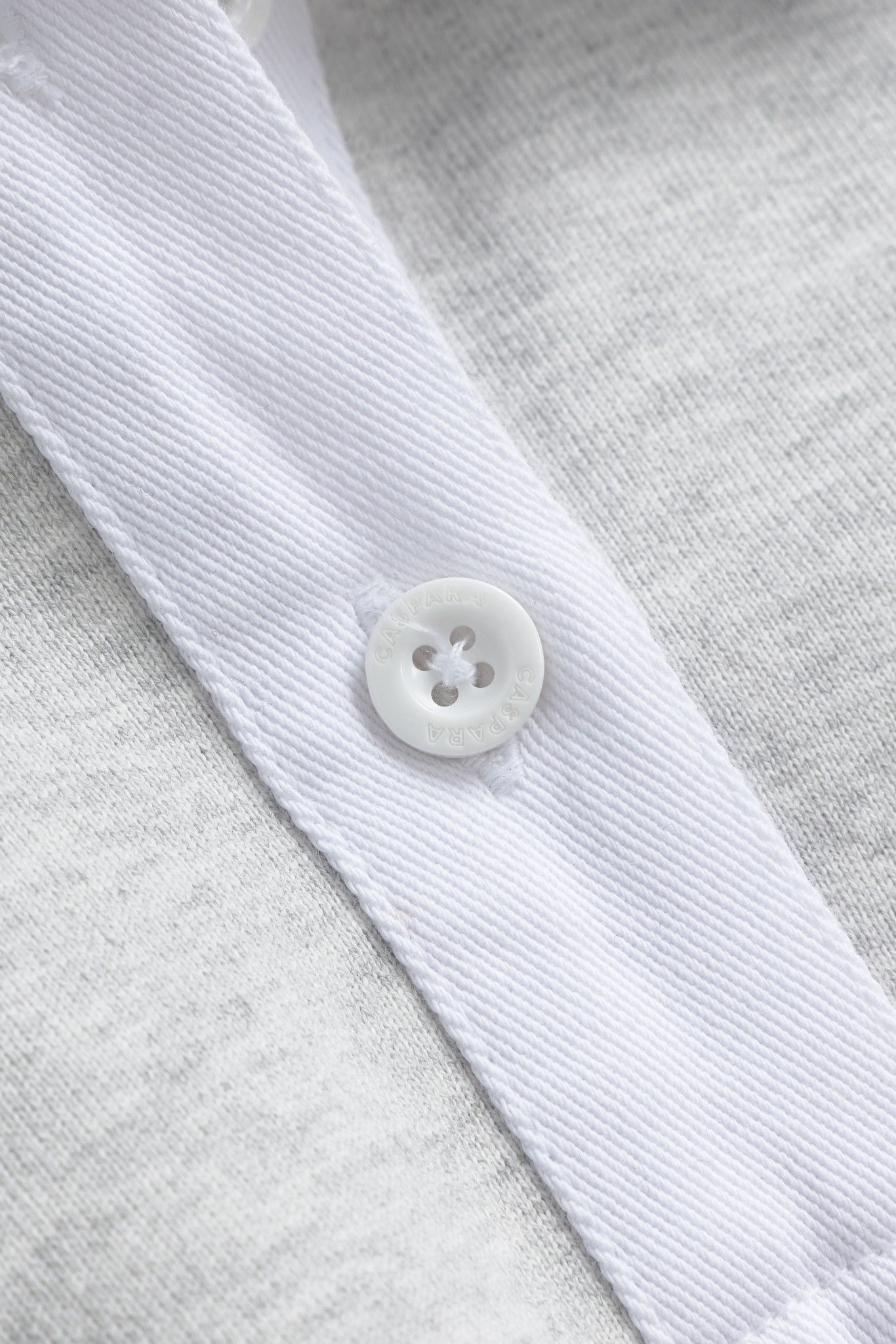 Close-up of the white placket and engraved CASPARA button on a grey rugby shirt.