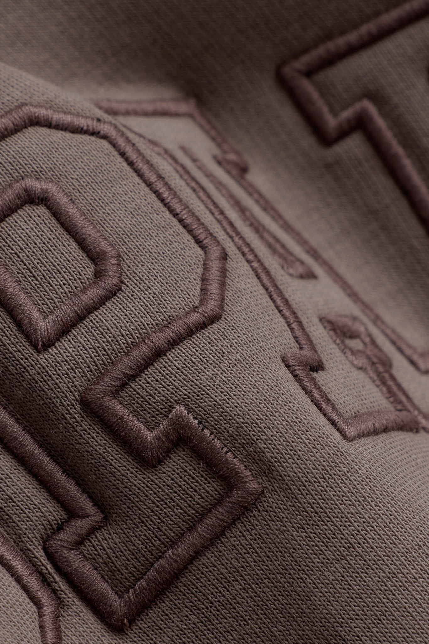 Close-up of tonal embroidered lettering on the walnut brown CASPARA All-Star hoodie.