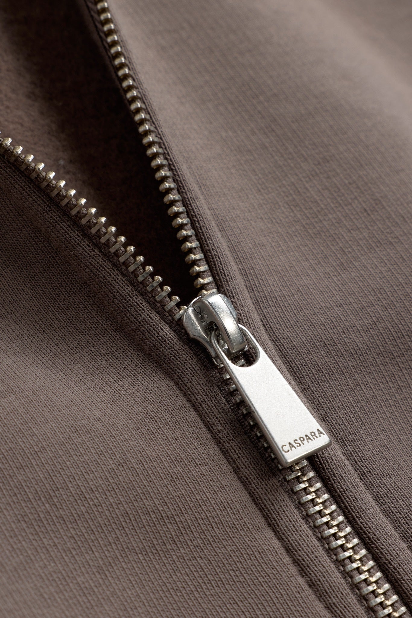 Close-up of the silver CASPARA logo zipper pull on a walnut All-Star zip hoodie.
