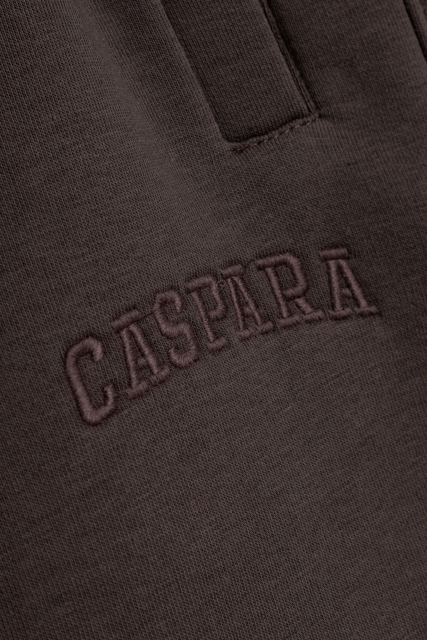 Detail of tonal embroidered CASPARA logo on espresso brown cotton sweatpants.