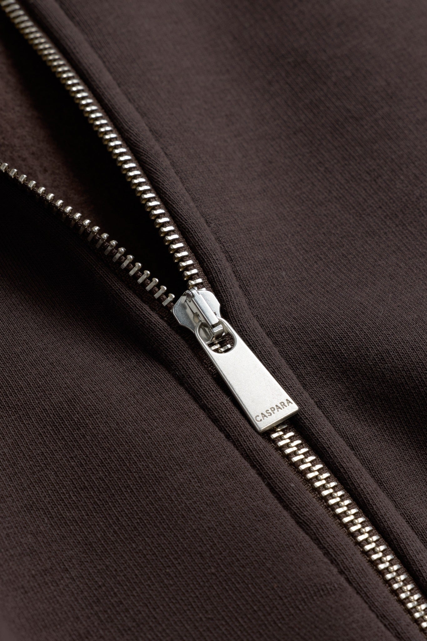 Close-up of a silver CASPARA engraved zipper pull on an espresso brown sweatshirt.