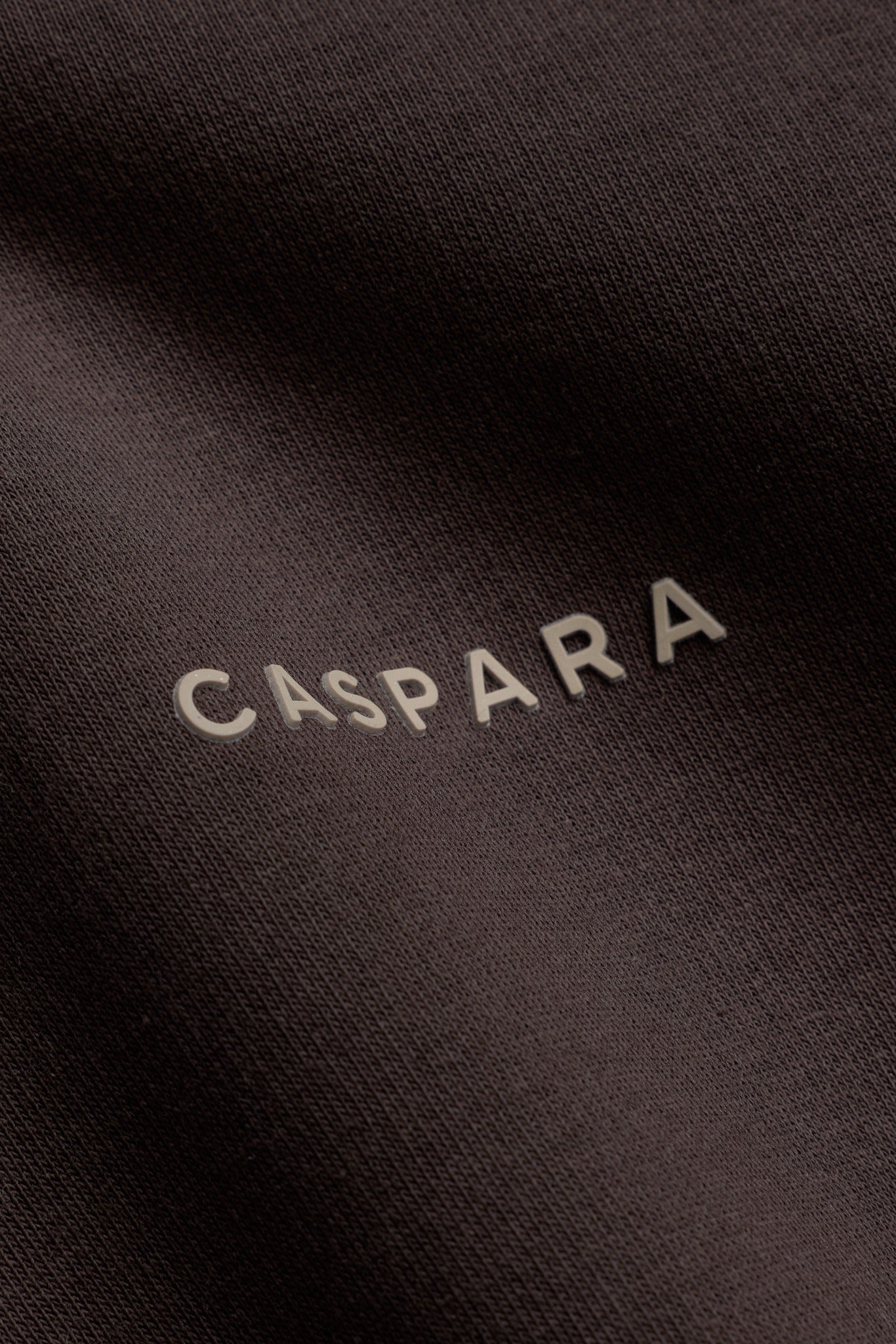 Close-up detail of the raised CASPARA logo on an espresso brown sweatshirt.