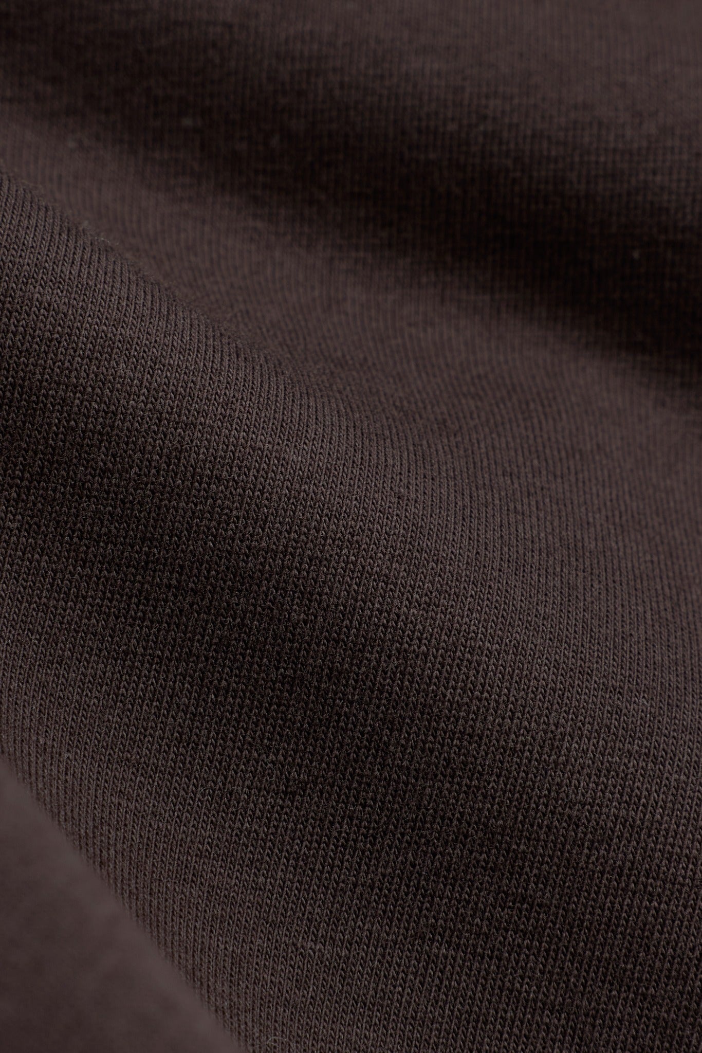 Close-up texture of espresso brown stretch jersey fabric on the CASPARA Baby Tee.