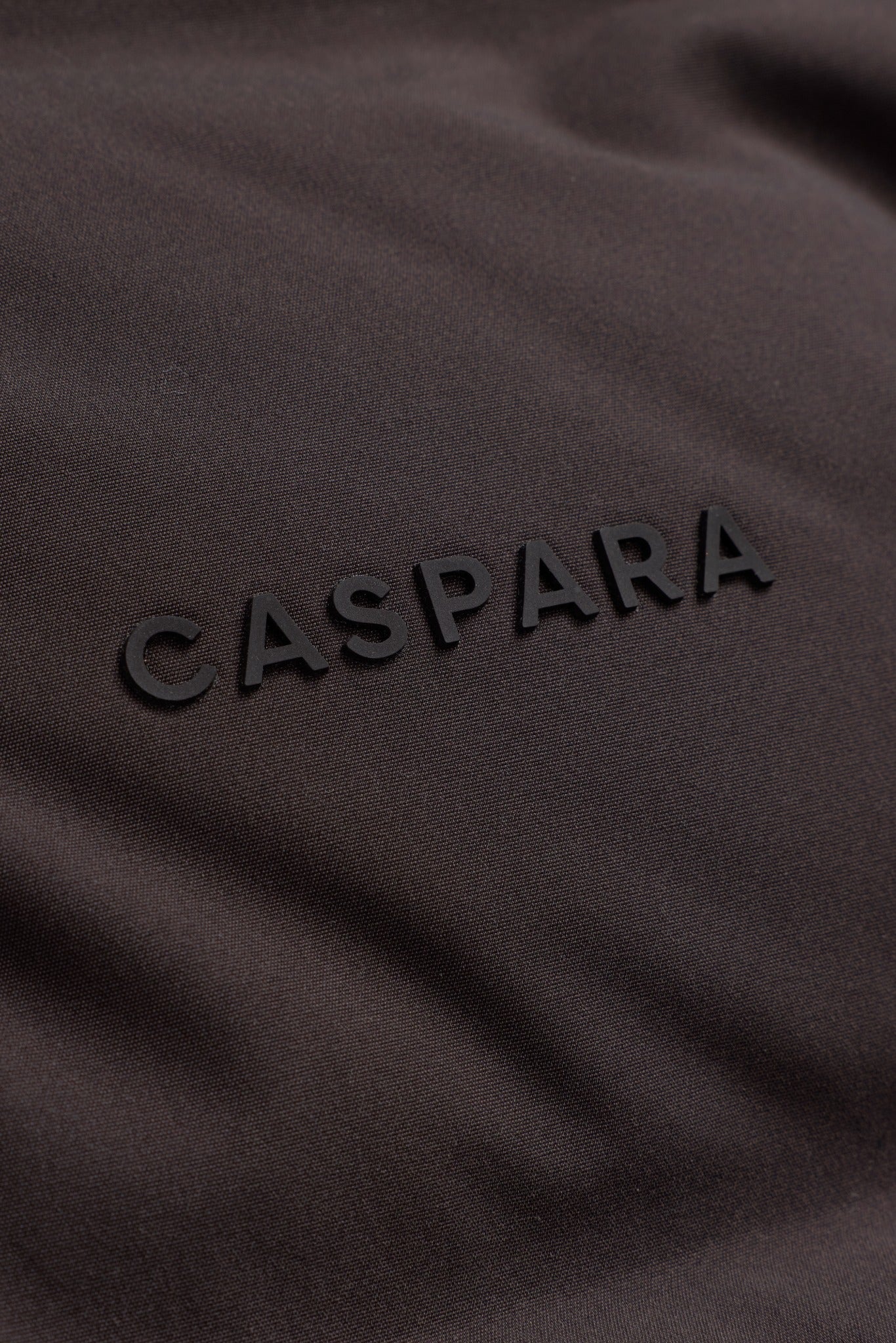 Close-up of the black raised CASPARA logo on an espresso Aurora Puffer Vest.