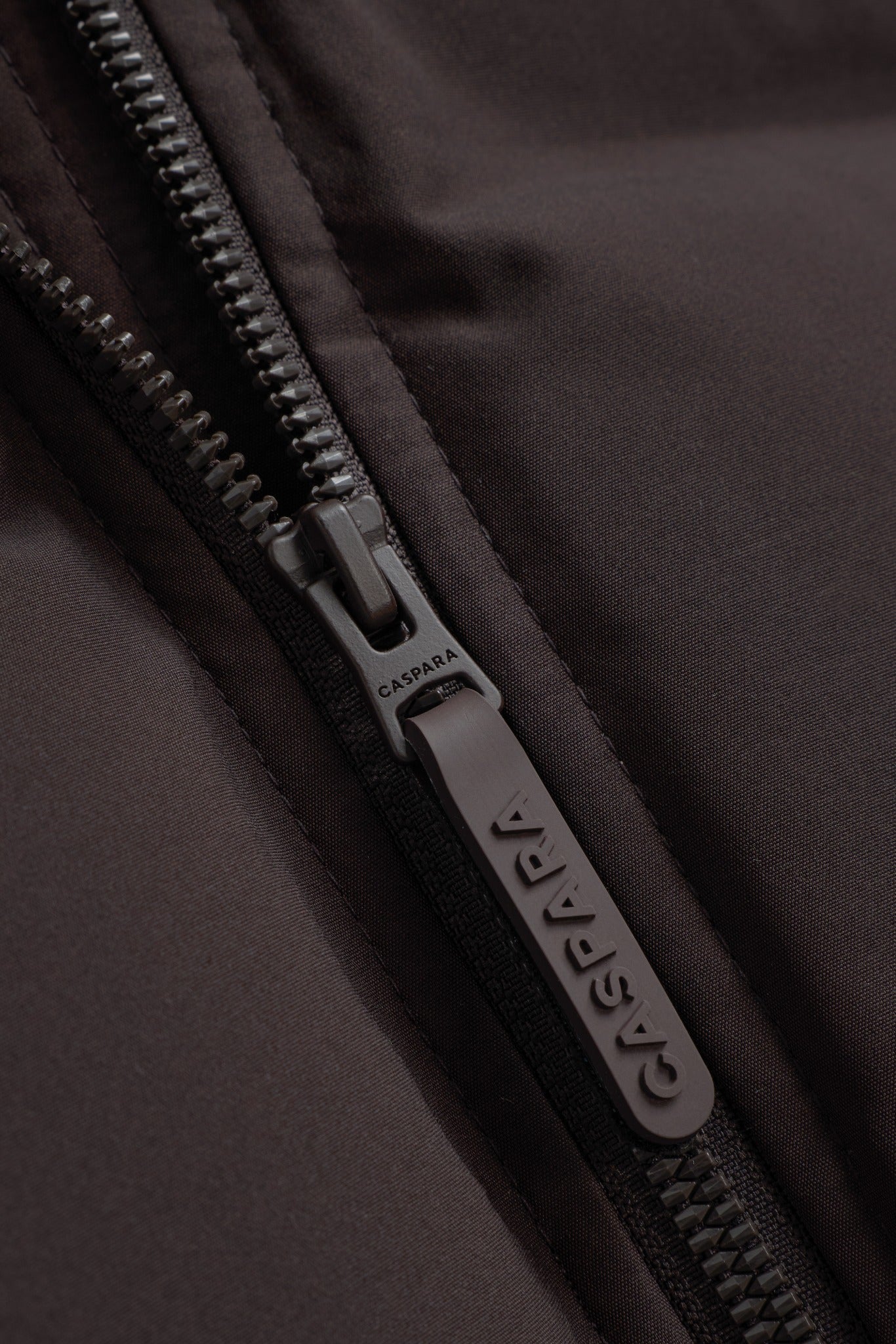 Close-up of the branded zipper pull on the espresso CASPARA Aurora puffer vest.