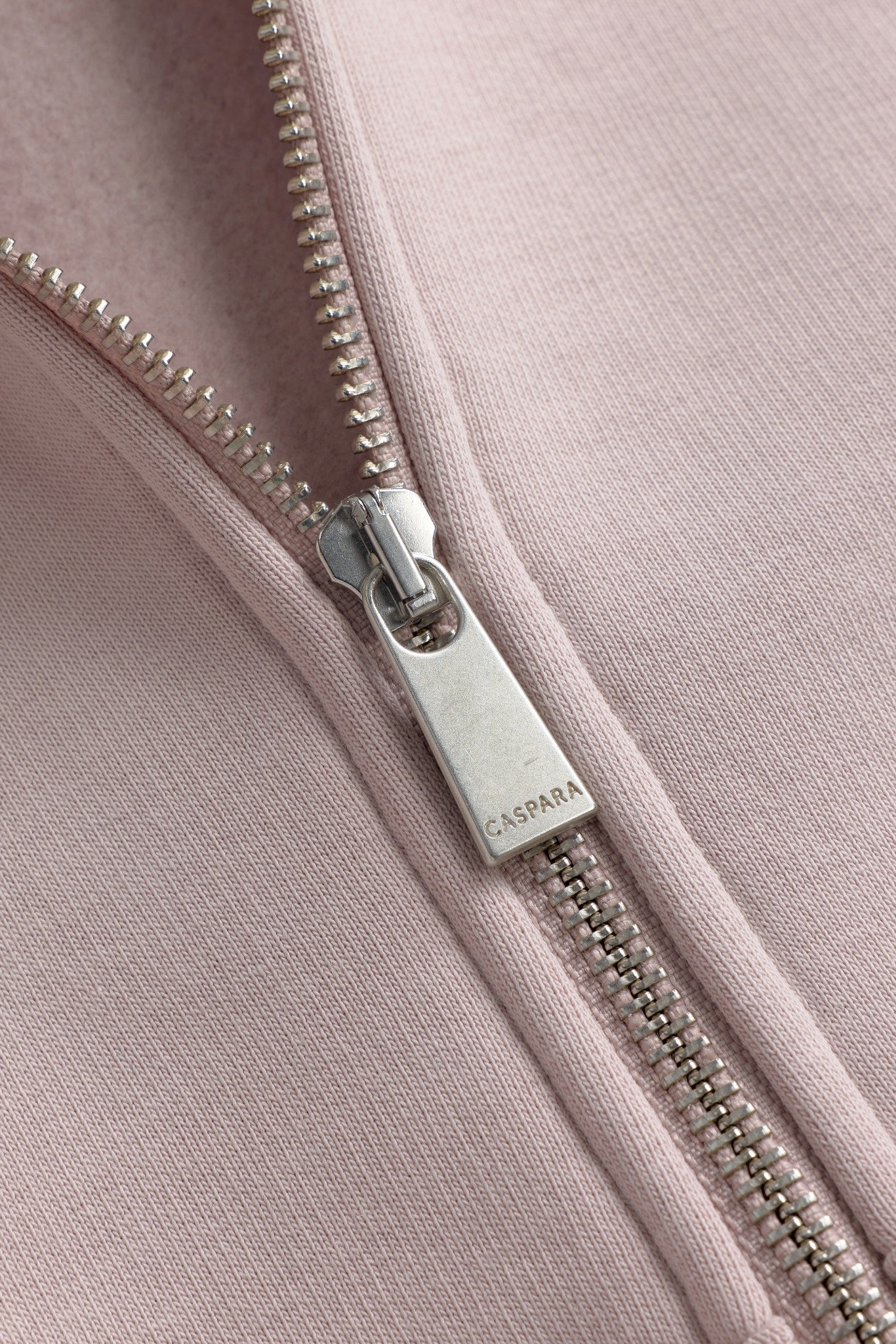 Close-up of the silver CASPARA logo zipper pull on a dusty pink zip-up hoodie.