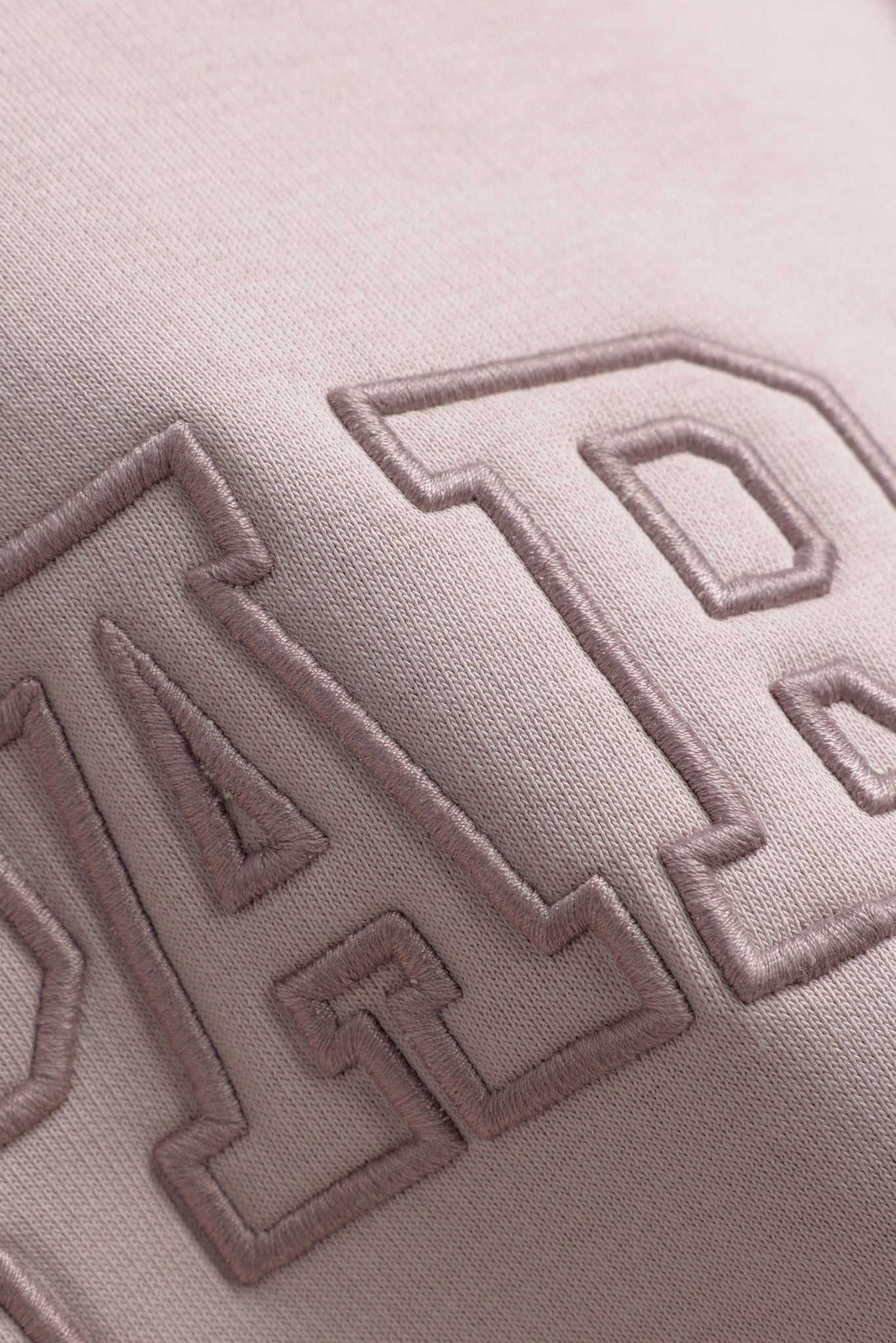 Close-up detail of embroidered outline logo on a dusty pink CASPARA crewneck sweatshirt.
