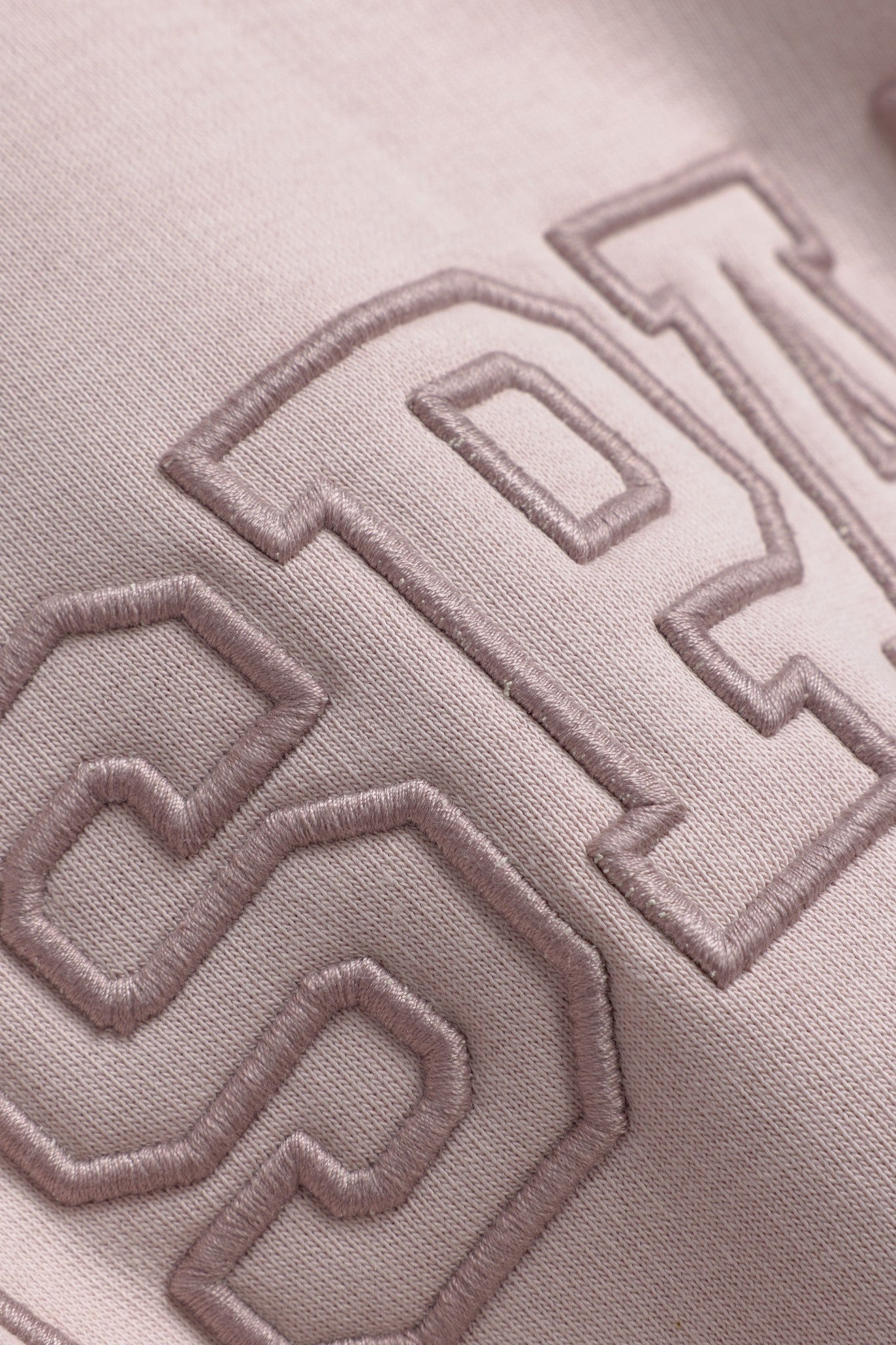 Close-up detail of embroidered lettering on a dusty pink CASPARA All-Star hoodie.