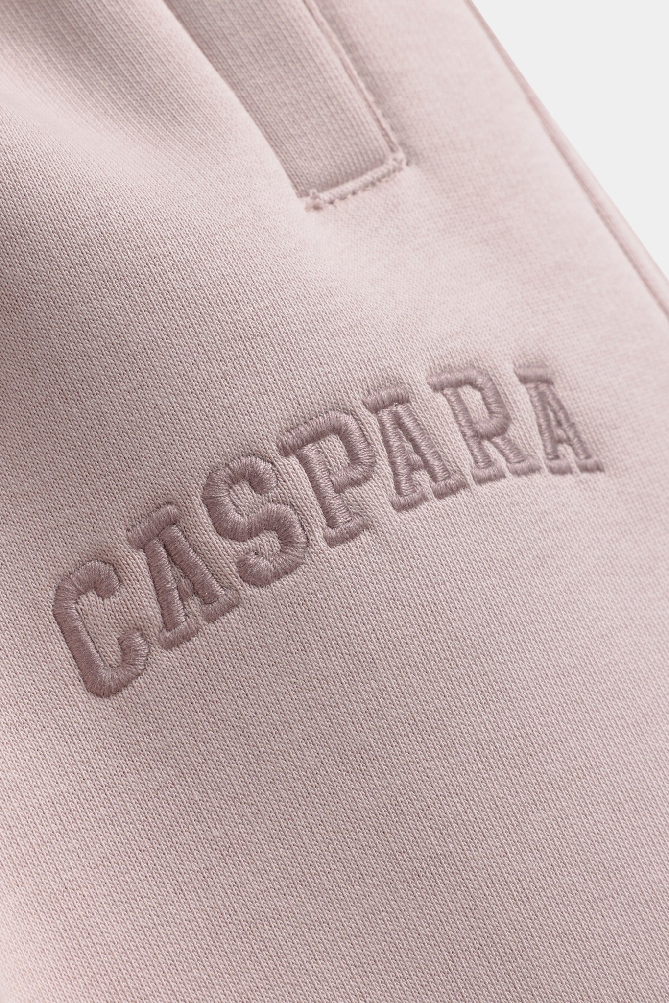 Close-up of embroidered CASPARA logo on dusty pink sweatpants.