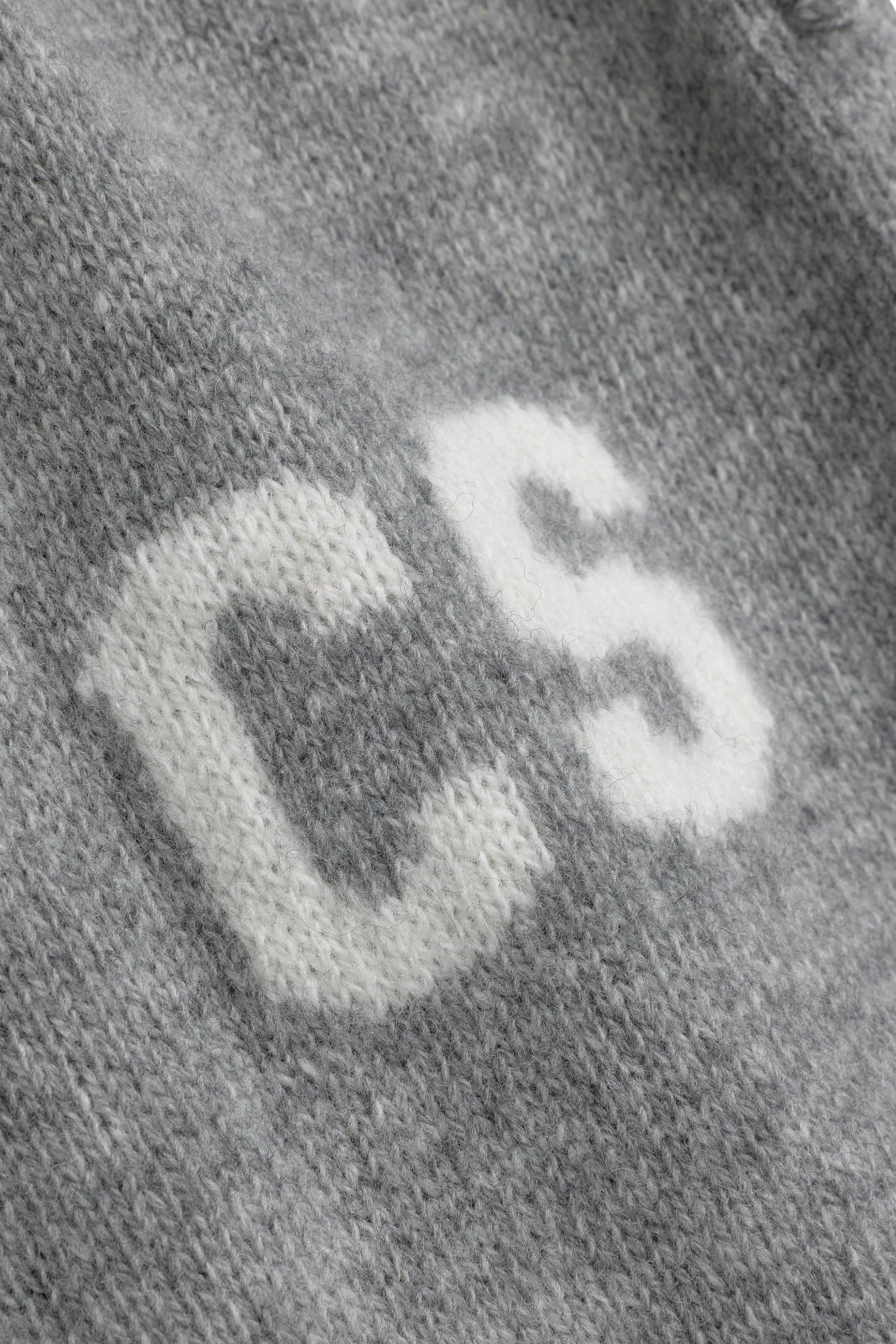 Close-up of grey woolknit pants featuring a white knitted CS logo detail.