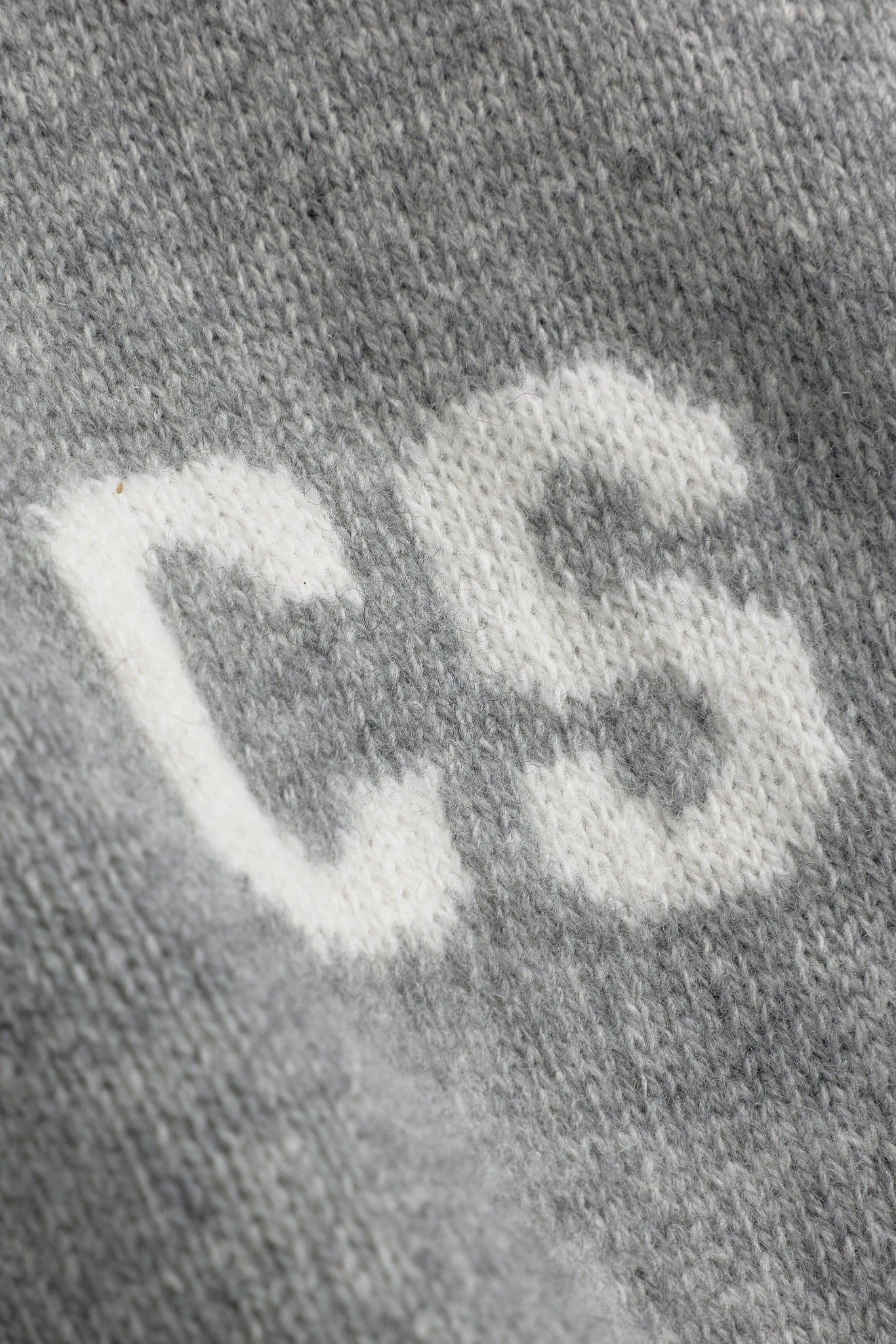 Close-up of the white knitted CS logo on a dark grey melange wool jacket.