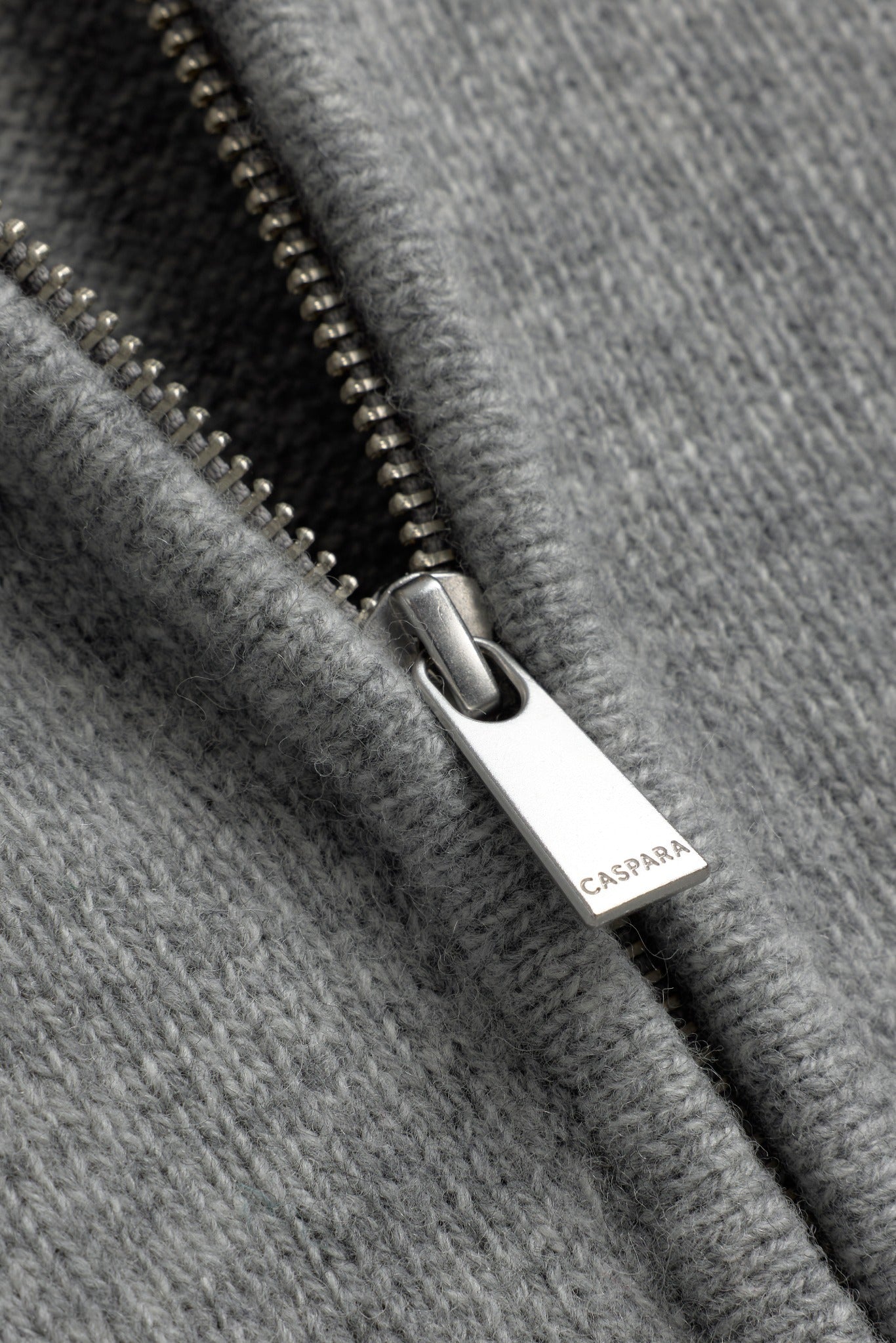 Close-up of the engraved silver CASPARA zipper pull on a dark grey woolknit jacket.