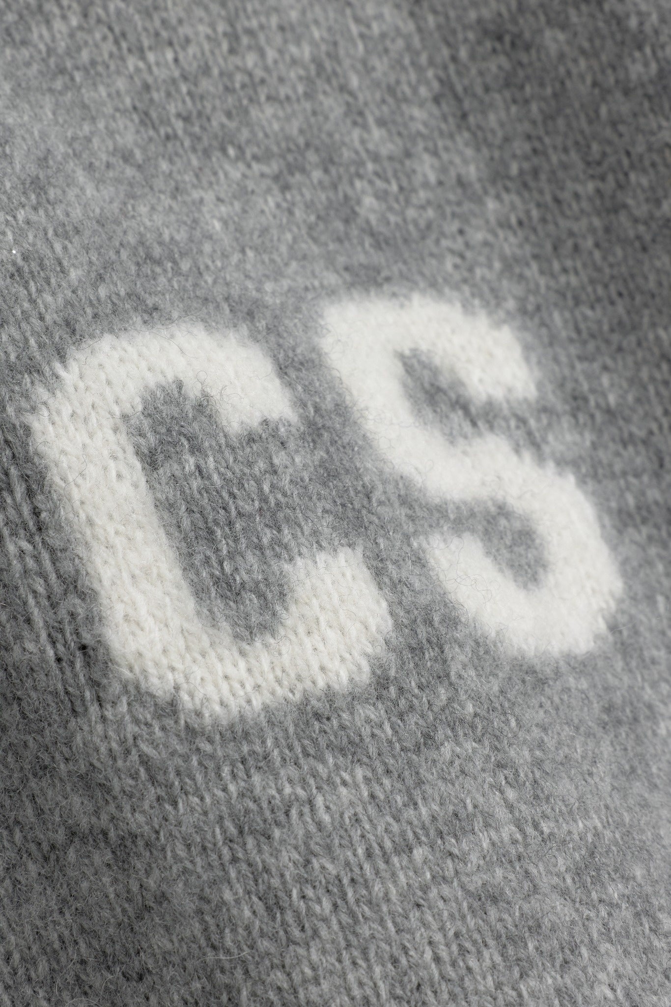 Close-up detail of white knitted CS logo on a grey wool CASPARA zip jacket.
