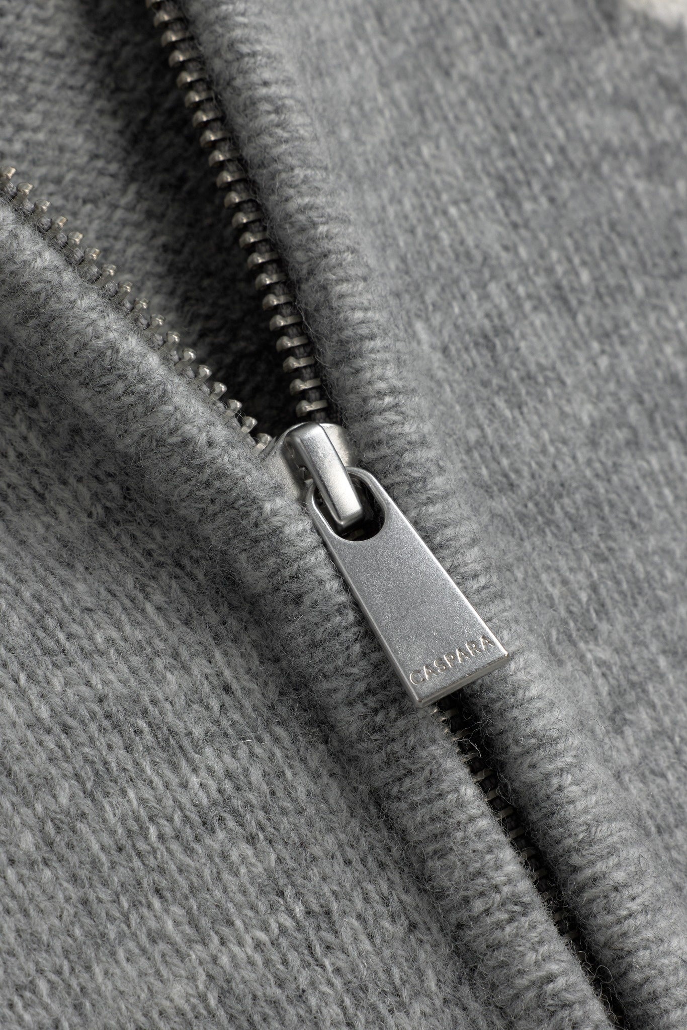 Close-up of the engraved CASPARA silver zipper pull on a grey wool knit jacket.
