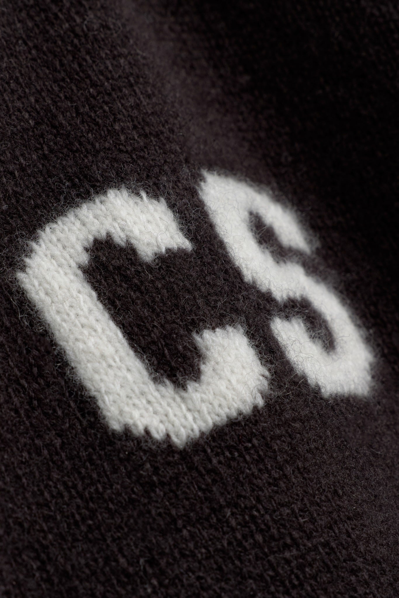 Close-up of the white knitted CS logo on a cocoa bean wool jacket.