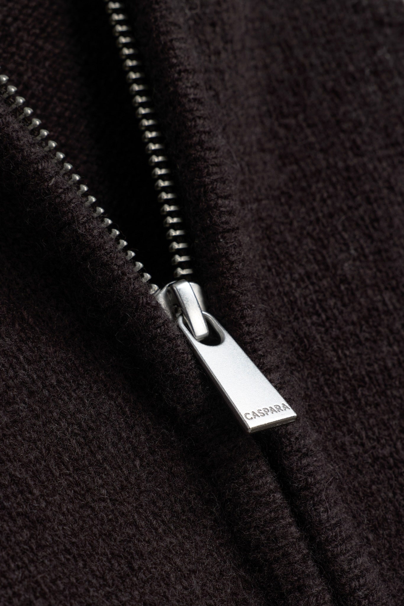 Close-up of the silver metal CASPARA logo zipper pull on a cocoa bean wool knit jacket.