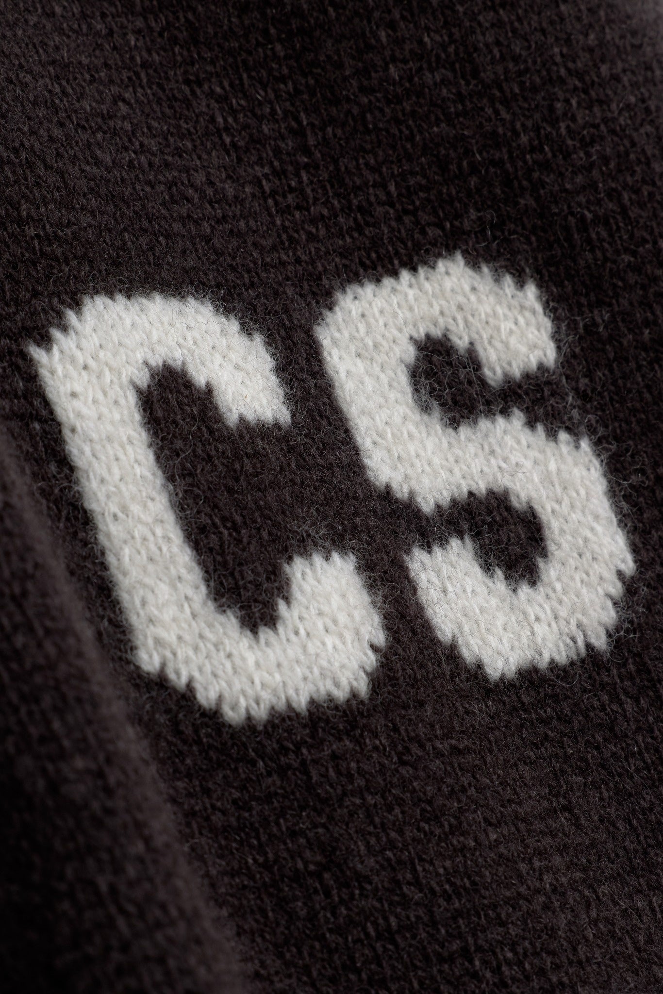 Close-up of the white knitted CS logo detail on cocoa bean wool knit pants.