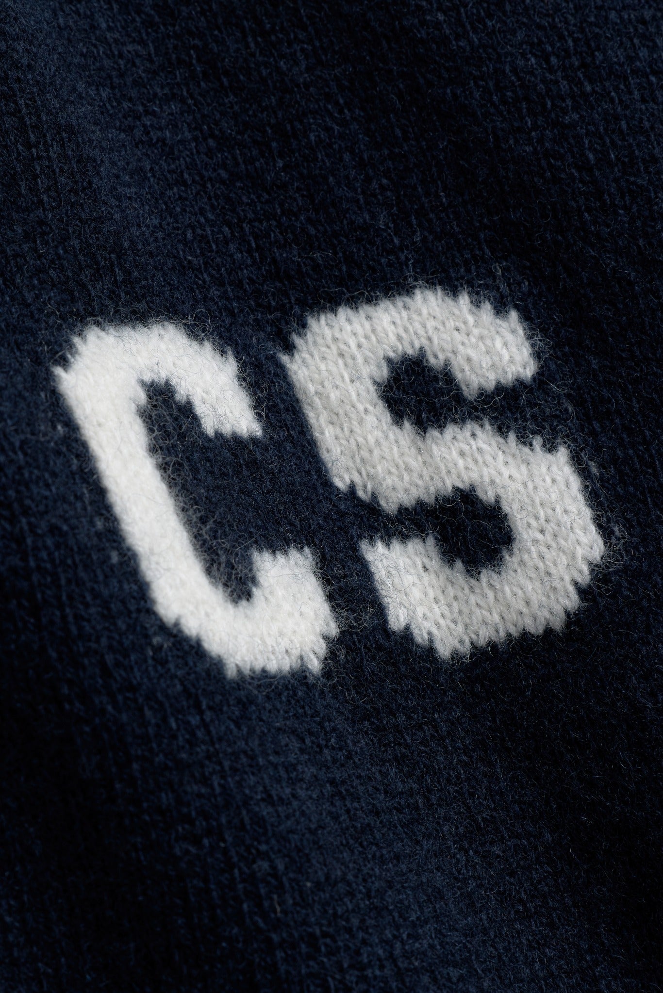 Close-up of the white CS monogram detail on a navy CASPARA wool knit jacket.