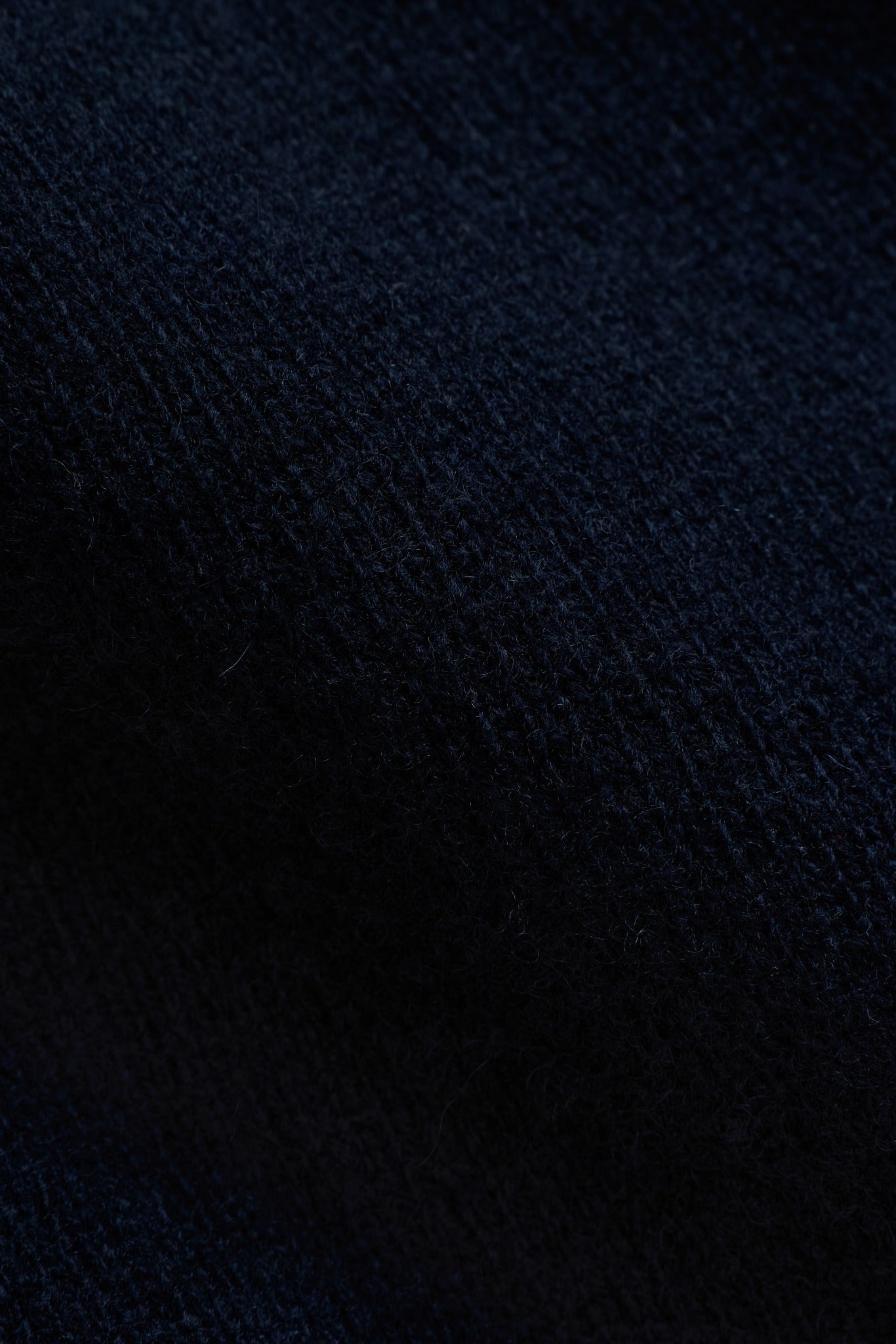 Close-up texture of navy blue wool knit fabric on a CASPARA jacket.