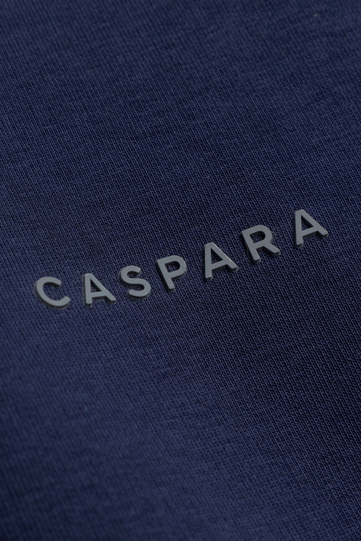 Close-up of the raised CASPARA logo on navy blue cotton sweatshirt fabric.