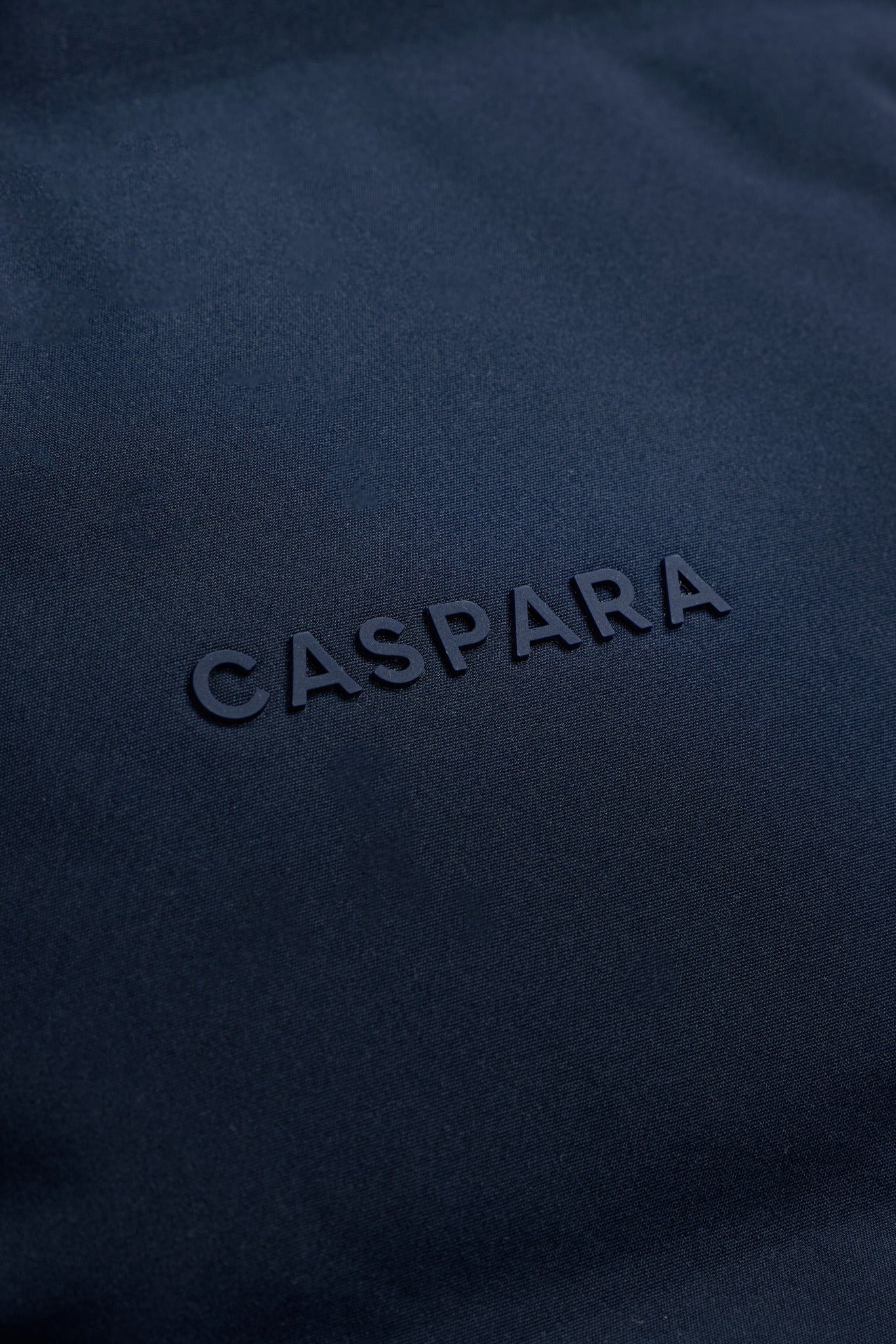 Close-up of the tonal CASPARA logo on the navy blue Boreal Puffer Vest fabric.