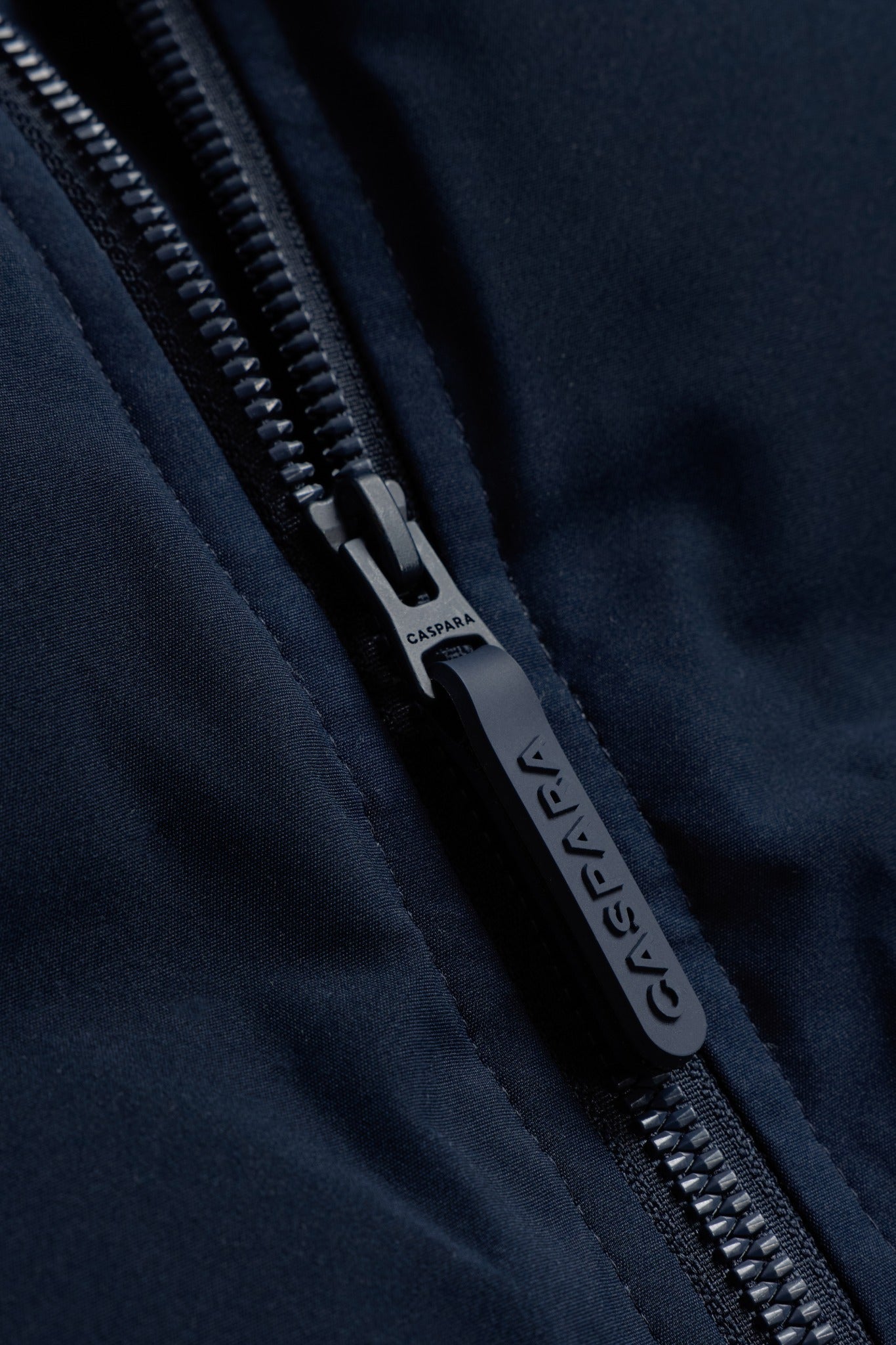 Close-up detail of the embossed CASPARA zipper pull on the navy Boreal puffer vest.