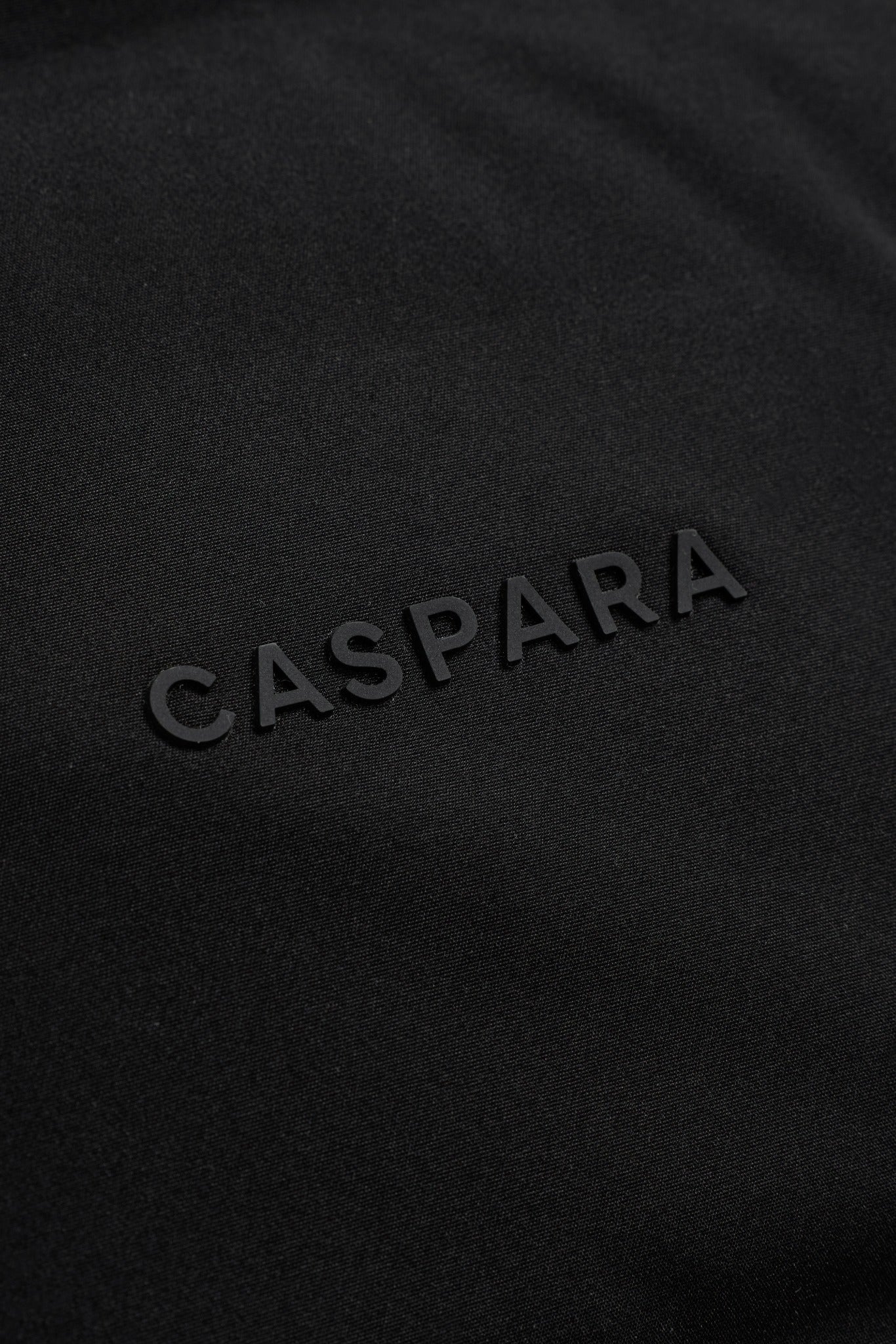 Close-up of the raised CASPARA logo on a black Boreal puffer vest.