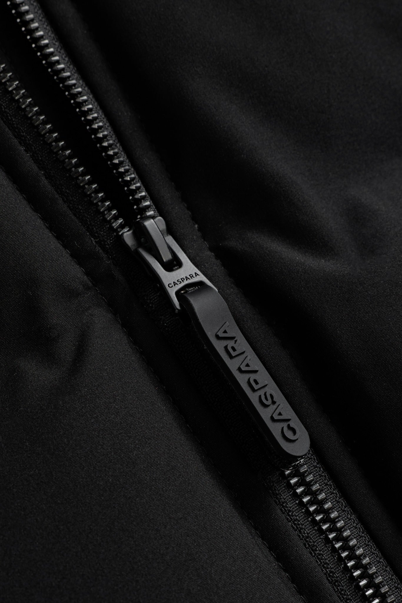 Close-up of the black zipper pull with embossed CASPARA logo on the Aurora puffer vest.