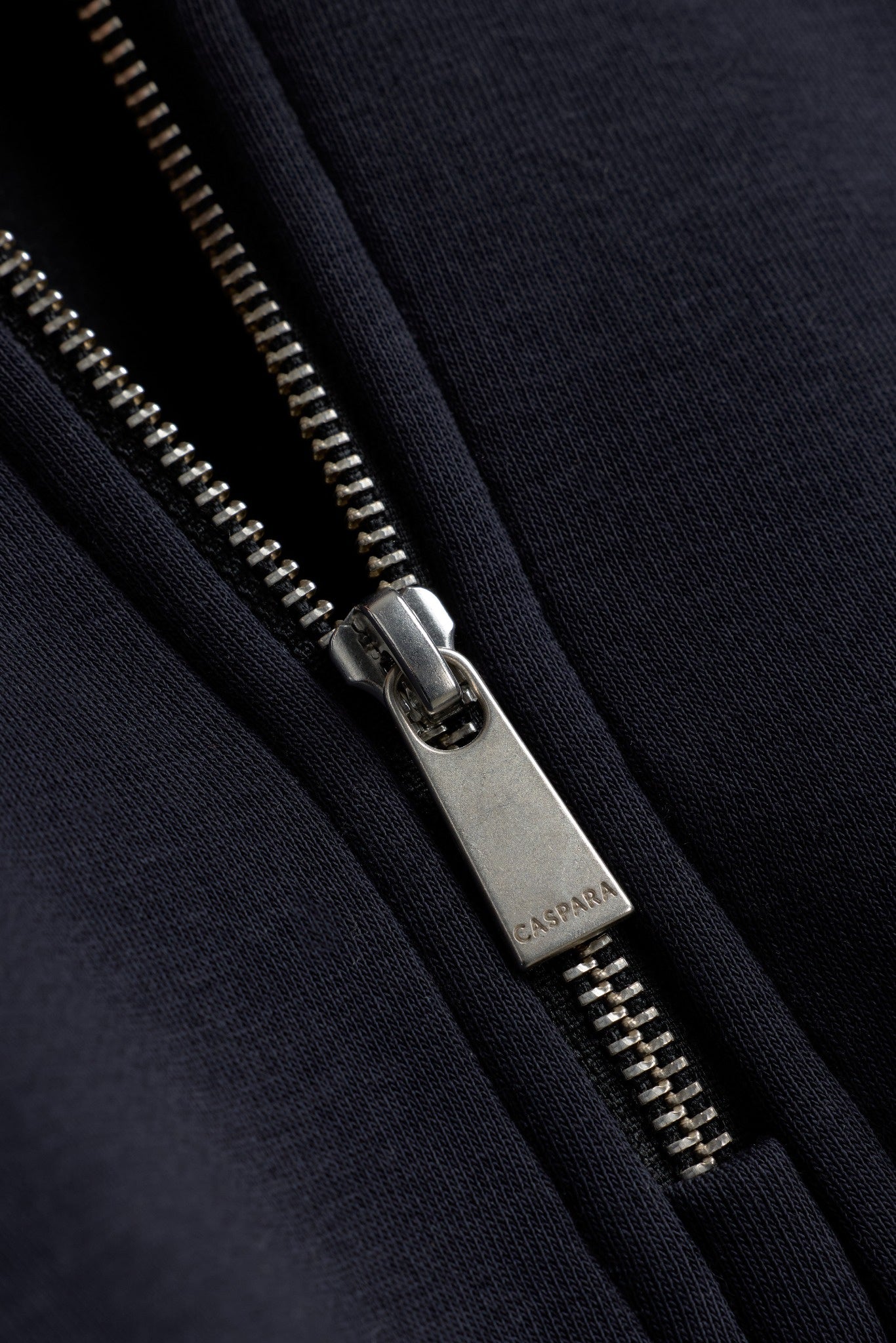 Close-up of the engraved metal zipper on the CASPARA Mineral Black 1/4 Zip sweatshirt.