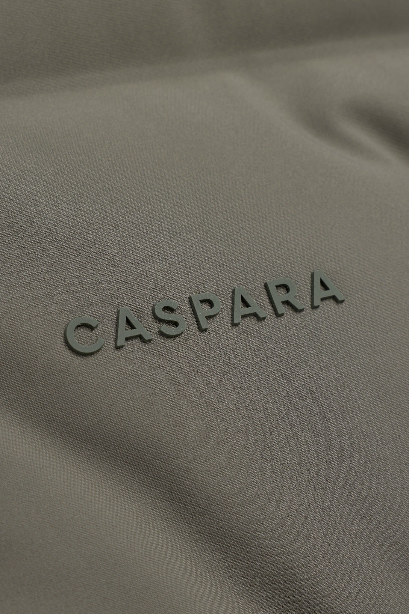 Close-up detail of the raised CASPARA logo on a khaki puffer vest.