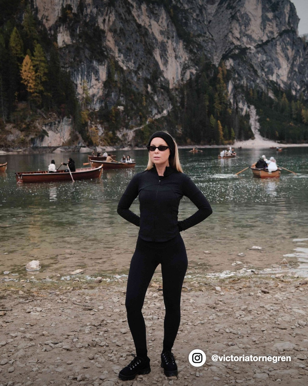 Woman wearing a black CASPARA Sculptluxe zip jacket standing by a mountain lake.
