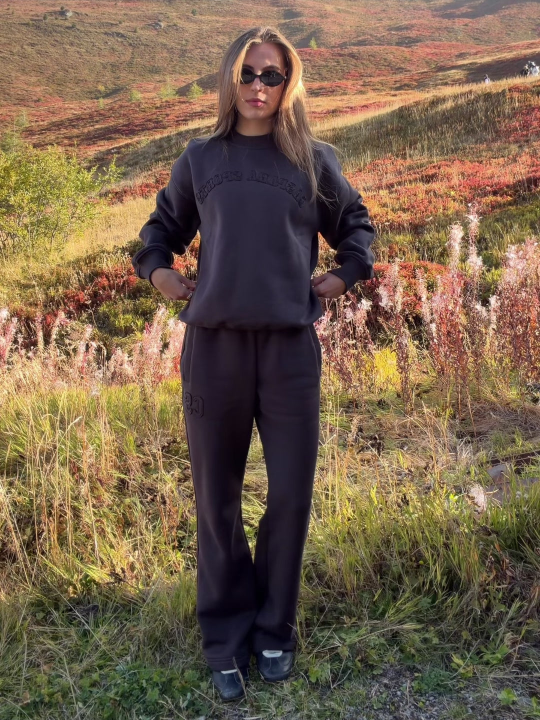 Woman wearing espresso CASPARA CS SL sweatpants standing on a grassy hillside.
