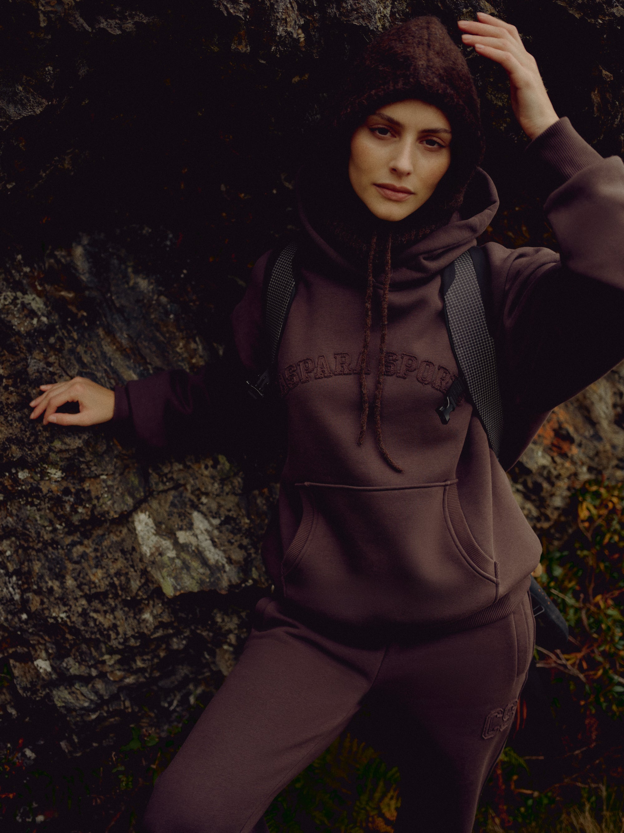 Woman wearing an espresso CASPARA CS hoodie standing against a rocky hillside.
